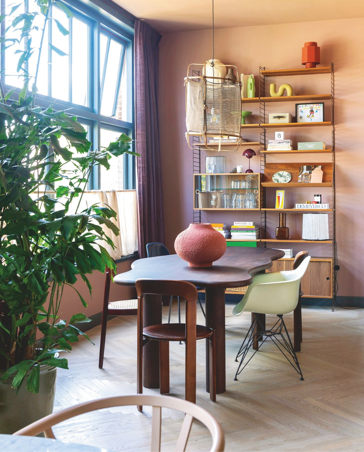 Kleur muur en plafond Nice Pink van The Nice Stuff Colours by Flexa x Karwei, kleur kozijnen Nice Night van The Nice Stuff Colours by Flexa x Karwei, houten vloer Vloerenhuis Amsterdam. Linnen gordijnen Evert Groot. Eettafel Table du Sud, stoel aan kopse kant Hay, witte stoel Vitra, vaas Theo-Bert Pot by Karwei, hanglamp Ay Illuminate. Kast String Furniture via Loft76, rode vaas Cor Unum via Drent & van Dijk, organische vaas HKliving. Auberginekleurige lamp &Tradition via Flow Lab Rotterdam, vaas rechts onderin kast Merci Parijs, tafellamp ernaast Gubi. vtwonen binnenkijken 09-2025 | styling en fotografie Theo Bert-Pot, Jelle van de Schoor | tekst Britte Kramer