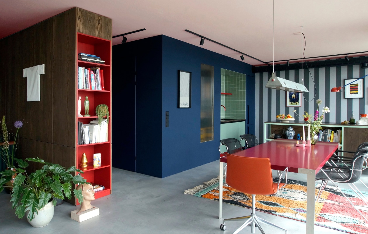 De kopse kant van de kastenwand is rood gelakt. Het grijs-zwart gestreepte behang was een restpartij. De tafel, stoelen en het tapijt zijn vintage. Stijlvol Wonen 8-2025 | Styling & Fotografie Bart Wigger | Tekst Evelien Roels