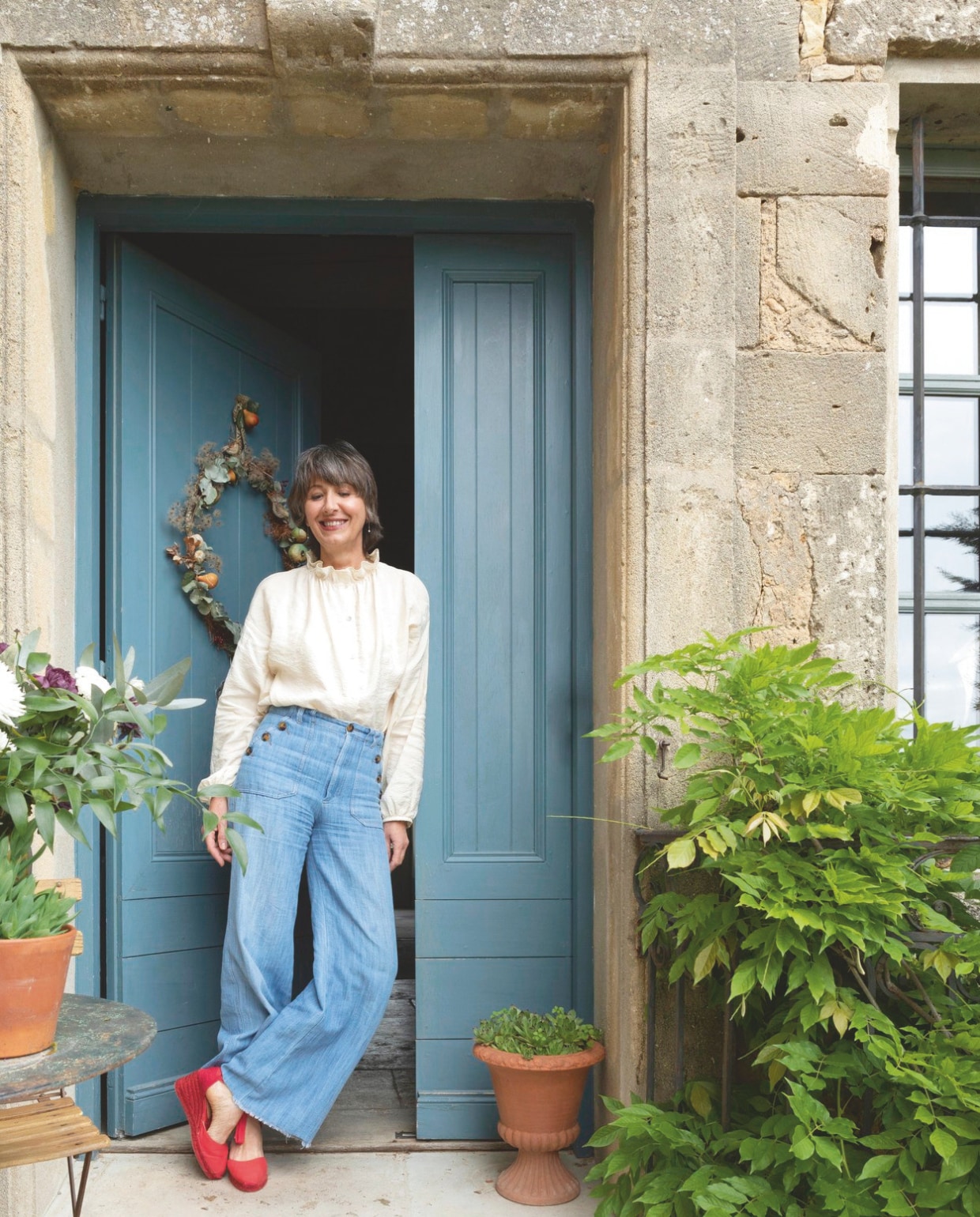 Sophie voor haar woning. De voordeur is geschilderd in dezelfde kleur blauw als de luiken. vtwonen Landelijk 8-2025 | styling Laura Taccari | fotografie Monica Spezia | tekstbewerking Roel Janssen
