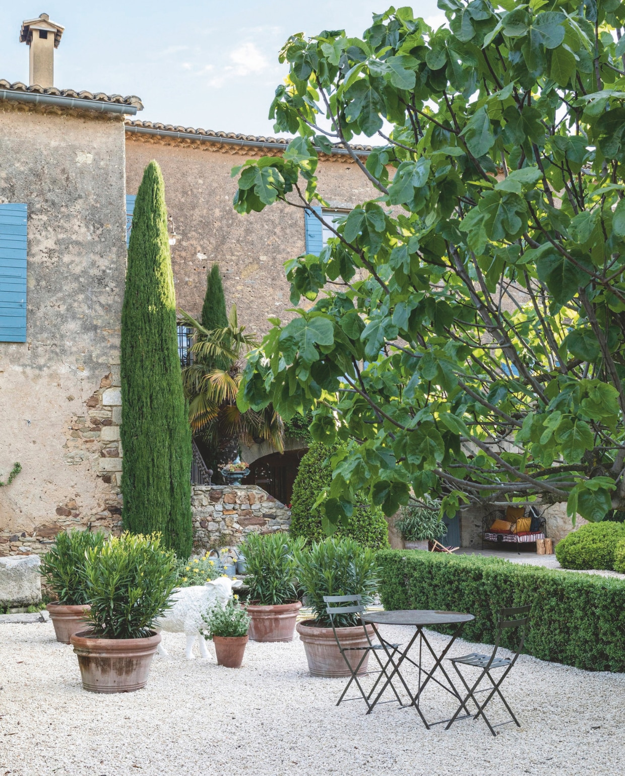De zuidgevel van het huis, met luiken in het typische blauw van de Cévennes. Vooraan een zitje en aardewerken potten van haar favoriete brocantewinkels. vtwonen Landelijk 8-2025 | styling Laura Taccari | fotografie Monica Spezia | tekstbewerking Roel Janssen