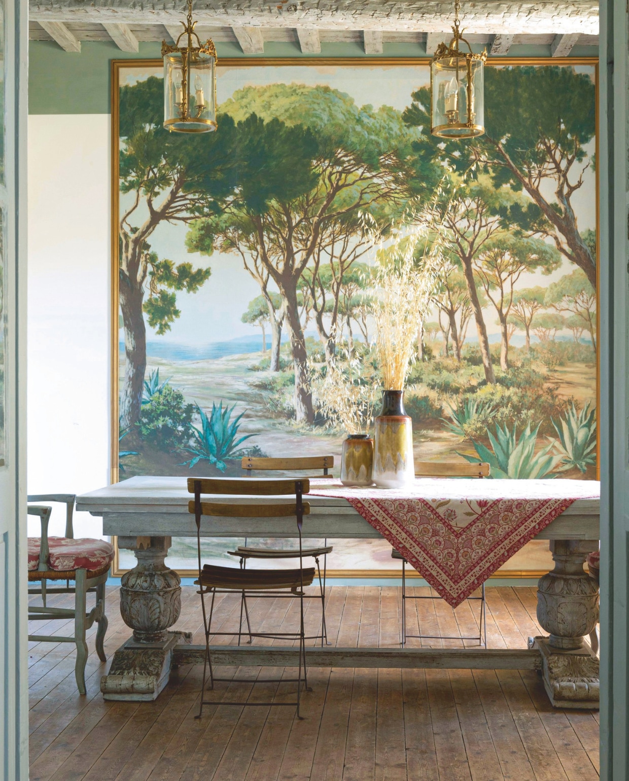 De eetkamer met panorama-behang L’Esterel van Pierre Frey, antieke eettafel en 18e-eeuwse tuinfauteuils. Vazen van Provençaals terracotta. vtwonen Landelijk 8-2025 | styling Laura Taccari | fotografie Monica Spezia | tekstbewerking Roel Janssen