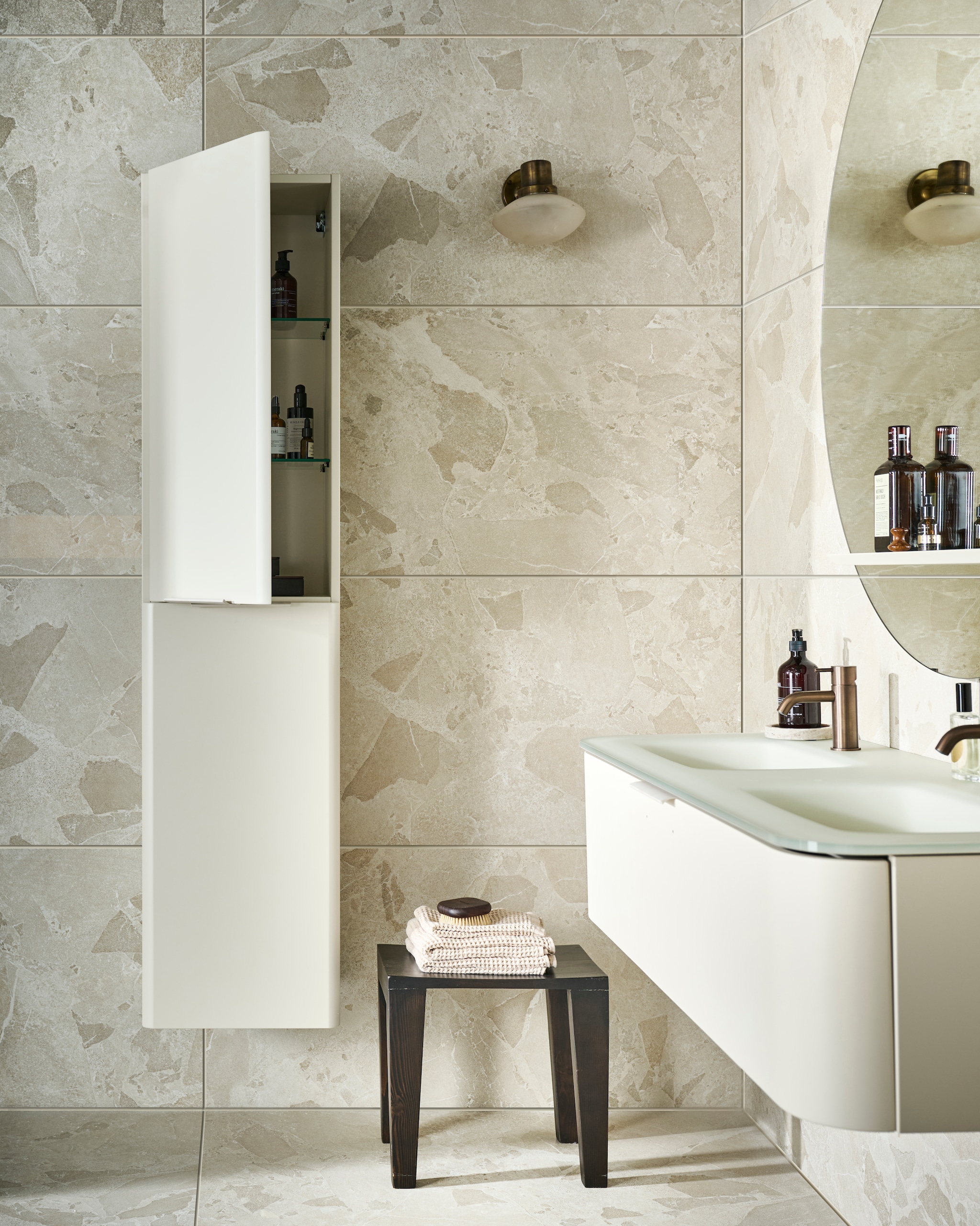 Kunststof kolomkast Bend met handgreep in matzand, 40x35,5x172 cm (bxdxh) € 1729,-, ook verkrijgbaar in zwart, grijs en wit. Glazen wastafel Soft Glas in matzand, 2 kraangaten en 2 waskommen, 131x48,5x1,2 cm (bxdxh) € 1634,-, ook verkrijgbaar in zwart, grijs en wit, met onderkast Bend in matzand, 1 lade met handgreep, 131x48,5x31 cm (bxdxh) € 1450,-, ook verkrijgbaar in matzwart, grijs en wit. Spiegel Reflect in zand, 120 cm (Ø) € 1198,-, ook verkrijgbaar in 80 cm (Ø) € 835,-. Op de wand: wand- en vloertegel Flakes Comet Cream, 60x120 cm, per m² € 69,50. Op de vloer: wand- en vloertegel Flakes Comet Cream, 120x120 cm, per m² 87,50. M.m.v. hotbath.nl (opbouwwastafelmengkraan Cobber CB003C), zarahome.com (vaas, kruk, handdoeken, kwarts), melchiorinterieur.nl (bijzettafel), merakimoments.com (marmeren dienbladen, zeepdispensers), linguaplanta.com (spray), pietjonker.nl (wandlamp), aesop.com (mondwater). Overig privébezit.