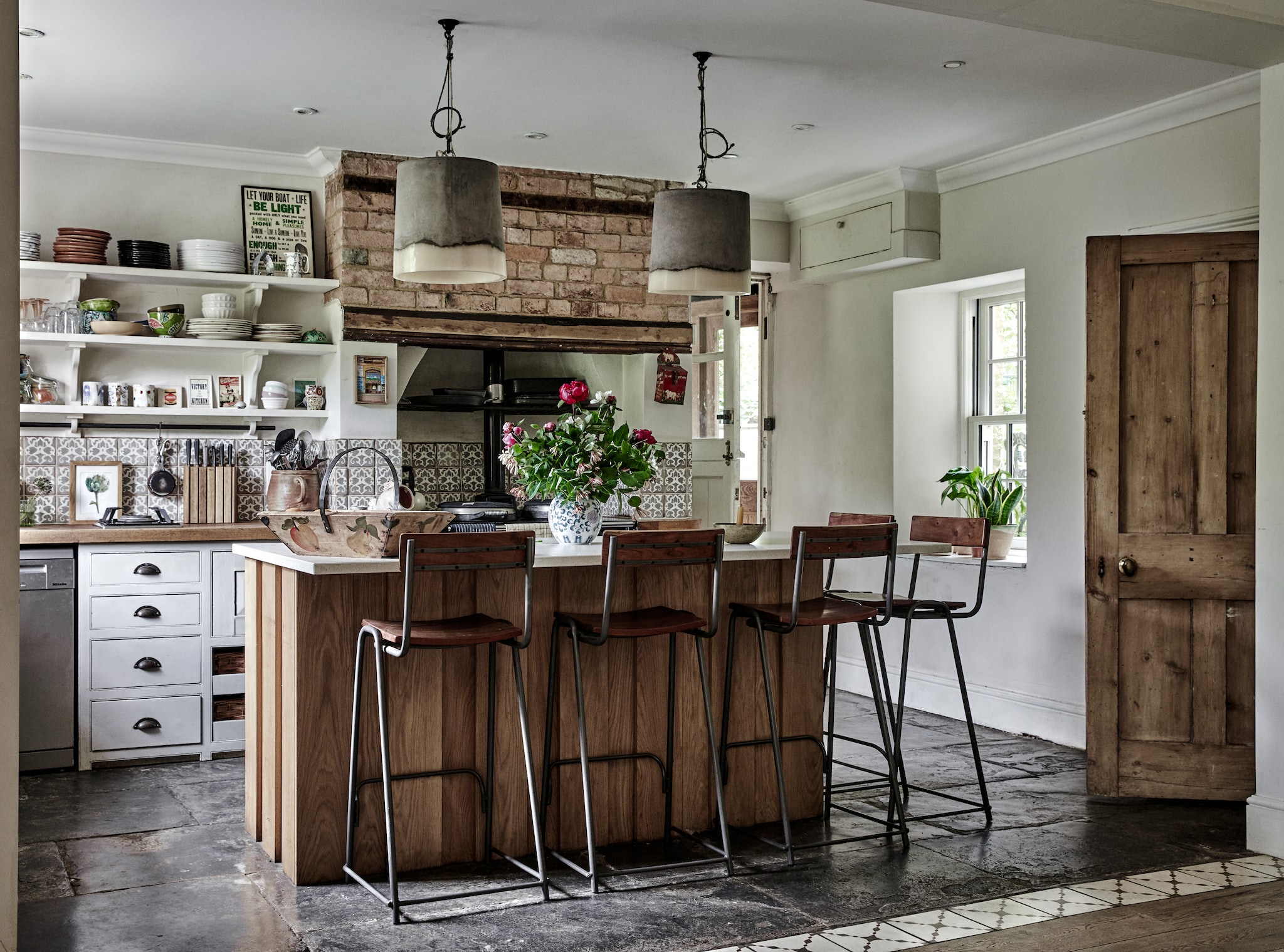 De bestaande keuken kreeg een nieuw, eiken eiland, gemaakt door een lokale timmerman. Barkrukken Rockett St. George. Hanglampen gevonden op een markt. De vloer en geschuurde deur zijn origineel. Wandtegels Fired Earth. De plek van een verwijderde tussenmuur is gemarkeerd met tegels van Bert & May. vtwonen Landelijk 12-2025 | productie Living Inside | fotografie Brent Darby
