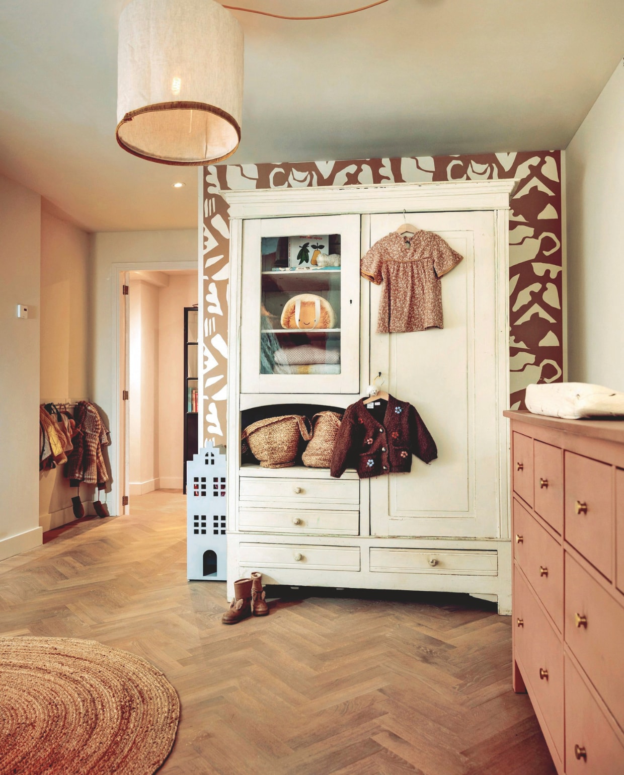 Lamp oude lamp gepimpt met bandje en gekleurd snoer. Behang Roomblush. Kast tweedehands. Huiskastje Hema. Manden H&M Home. Commode Ikea. Vloer De Houtfabriek.Kleed Boho & Me. vtwonen 10-2025 | fotografie Ernie Enkelaar | tekst Merel van der Lande