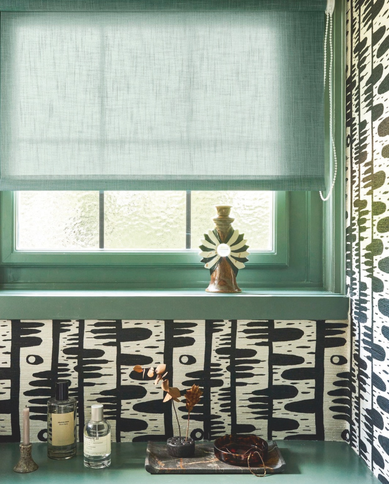 vtwonen rolgordijn, lichtdoorlatende stof, structuur, zeegroen (nr. 18017), vanaf  € 112,37.M.m.v. zarahome.com (kandelaar), pierrefrey.com (behang Tehea). Overig privébezit. vtwonen 10-2025 | styling Kim van Rossenberg | fotografie Sjoerd Eickmans