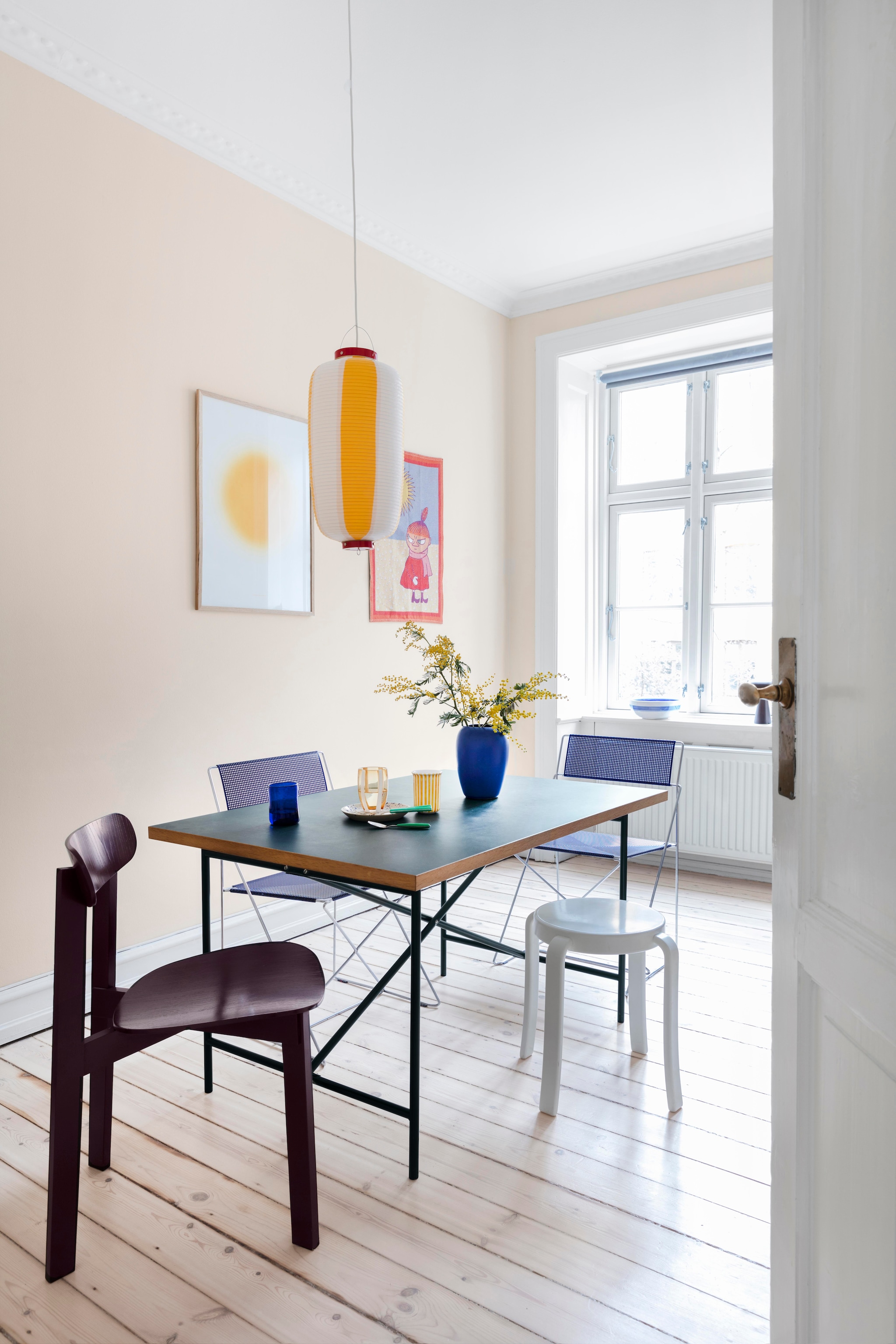 Eettafel van Egon Eiermann. Stoelen X-line van Niels Jørgen Haugesen. Auberginekleurige stoel Please wait to be seated. Kruk 8000 van Magnus Olesen. Hanglamp cadeau gekregen uit Japan. Vintage vaas Holmegaard. Beker erfstuk van Amalie’s oma. Glas Zafferano Italia. Poster Ace & tate X Playtype. Illustratie Little my van Tove Jansson. vtwonen 01-2026 | productie Living Inside | styling Rikke Graff Juel | fotografie Christina Kayser O.