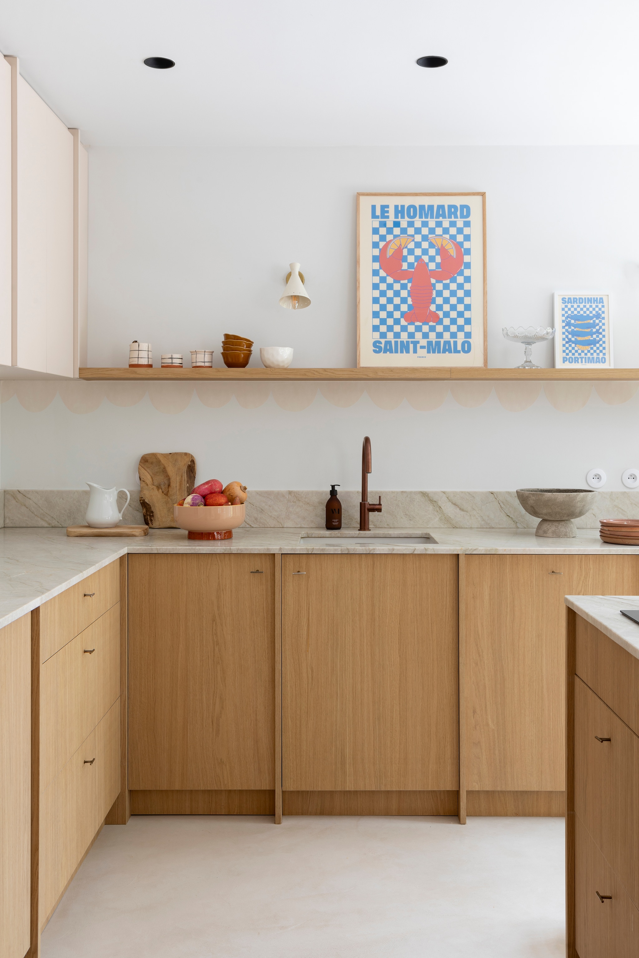 Kastfronten en planken Unilin. Aanrecht en achterwand in Taj Mahal graniet van Passion Granit. Kraan Treemme. Krukken Sklum. Witte wandlampen Selency. Slakom, houten plank, geruit servies en vaas Les Puces du Canal. Bruine kommen Søstrene Grene. Poster kreeft Poils Plumes Art. Keukenkasten ontworpen door Charlotte, uitgevoerd door B.i concept. vtwonen 01-2026 | styling Marie Maud Levron | fotografie Pierrick Verny | productie AC Scoffoni