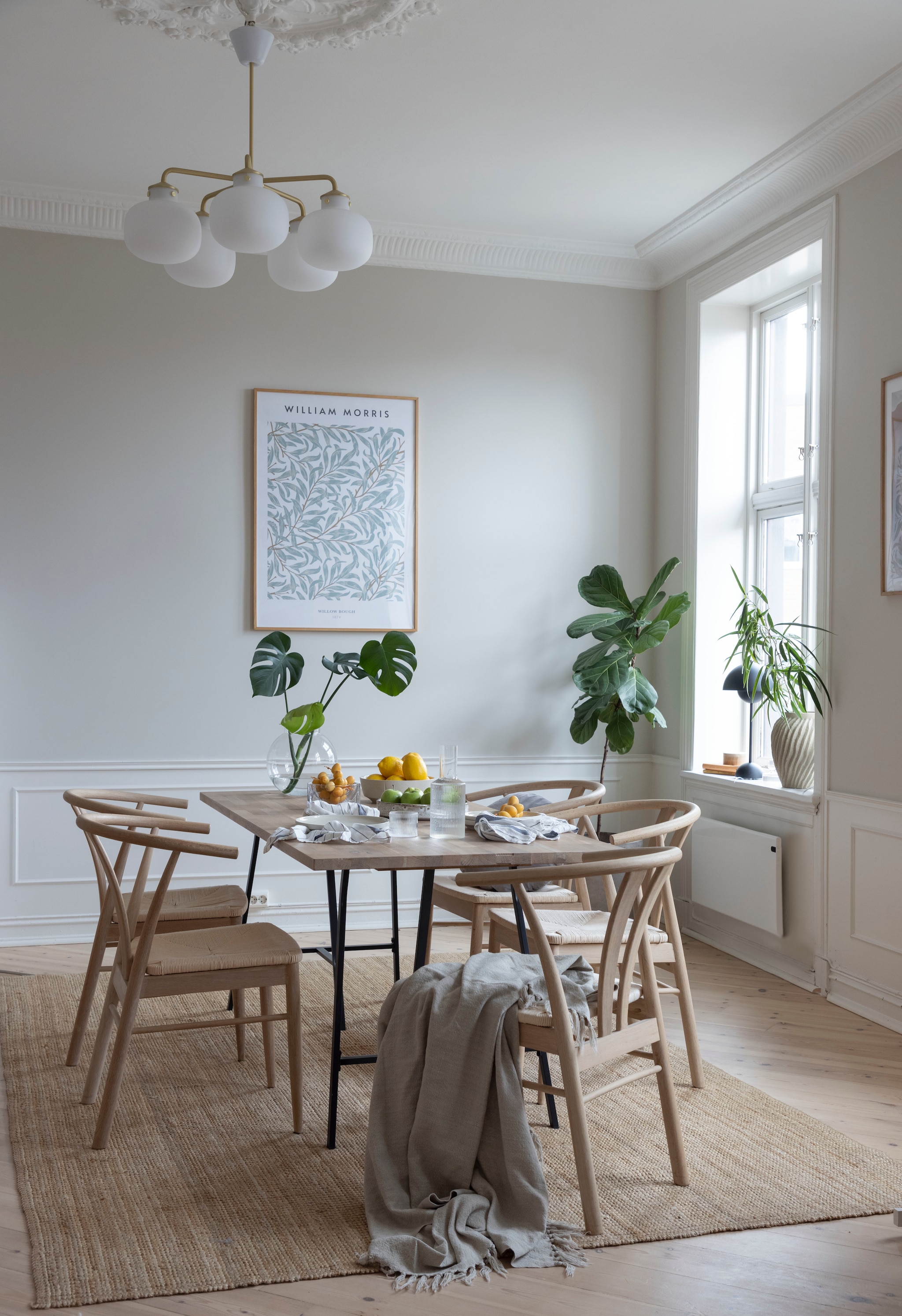 Eettafel zelf gemaakt. Stoelen van Møbelringen gekocht op tweedehandsplatform Tise, een alternatief is de CH24 Wishbone chair van Hans Wegner voor Carl Hansen. Print Desenio. Hanglamp Raito van Nordlux. Vloerkleed Strög van Ikea. De haard is origineel. vtwonen 01-2026 | styling Mari K. Olsen | fotografie Filippa Tredal | productie House of Pictures