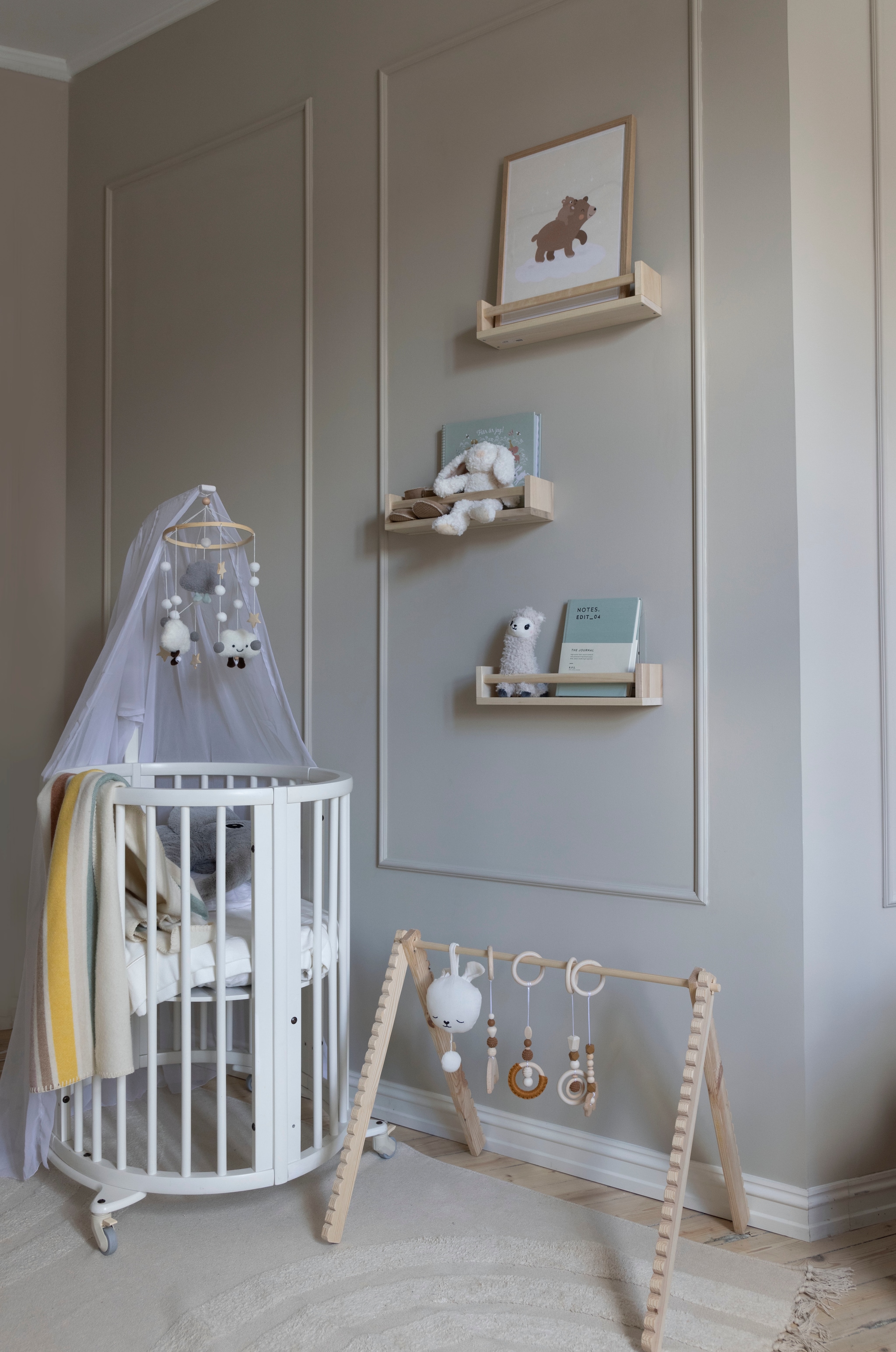 Ledikant Sleepi inclusief hemel van Stokke. Wandplanken Wekväm van Ikea. Soortgelijke houten baby gym en mobile Jollein. Vloerkleed H&m Home. Wandkleur Sand van Jotun. vtwonen 01-2026 | styling Mari K. Olsen | fotografie Filippa Tredal | productie House of Pictures