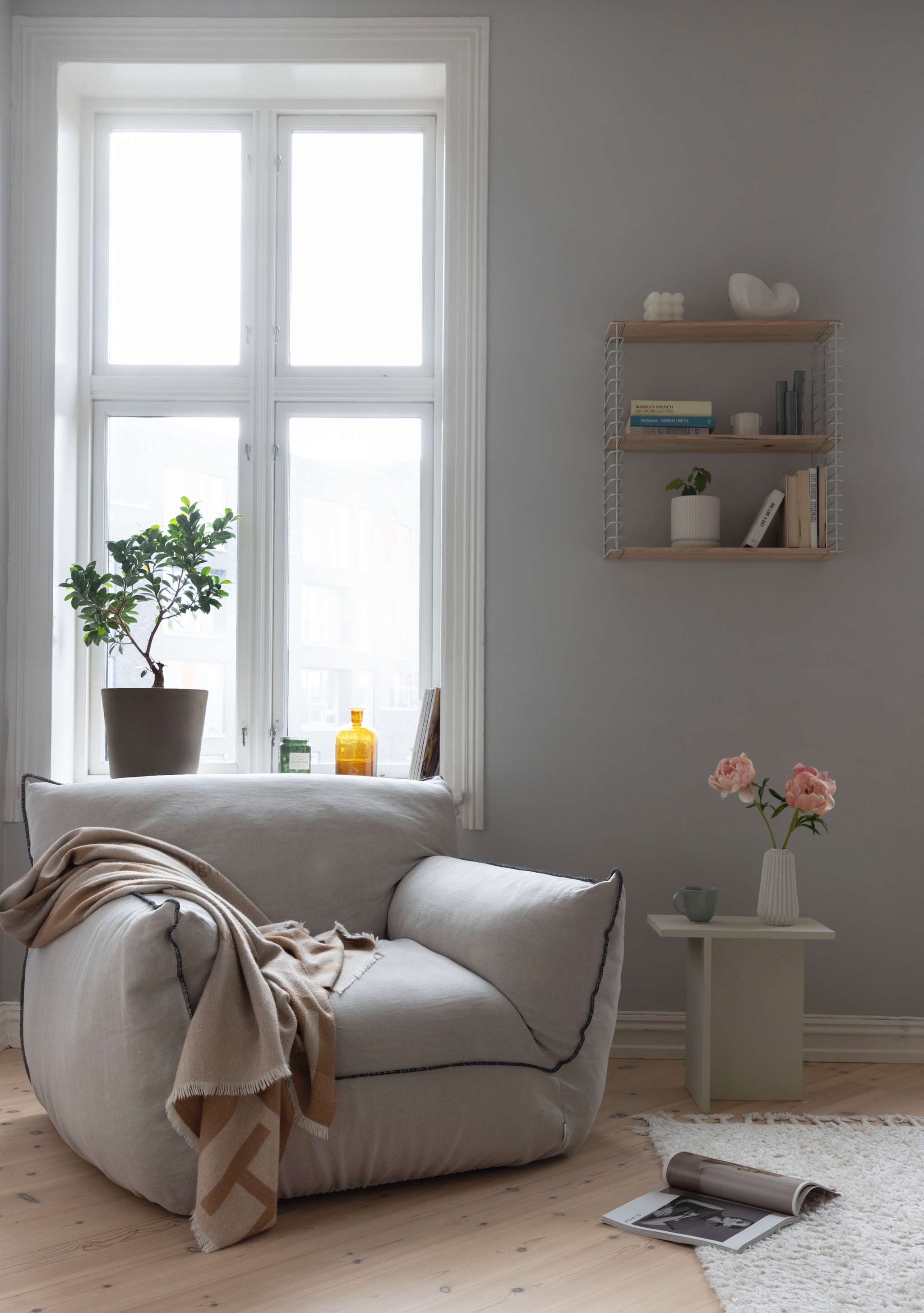 Linnen fauteuil Gia van Pastill. Bijzettafel zelf gemaakt. Wandrek Kristin van Kremmerhuset, geïnspireerd op systeem van String furniture. Nora zette gekleurd glaswerk van een rommelmarkt op de vensterbank, omdat het ’t natuurlijke licht zo mooiweerkaatst. vtwonen 01-2026 | styling Mari K. Olsen | fotografie Filippa Tredal | productie House of Pictures