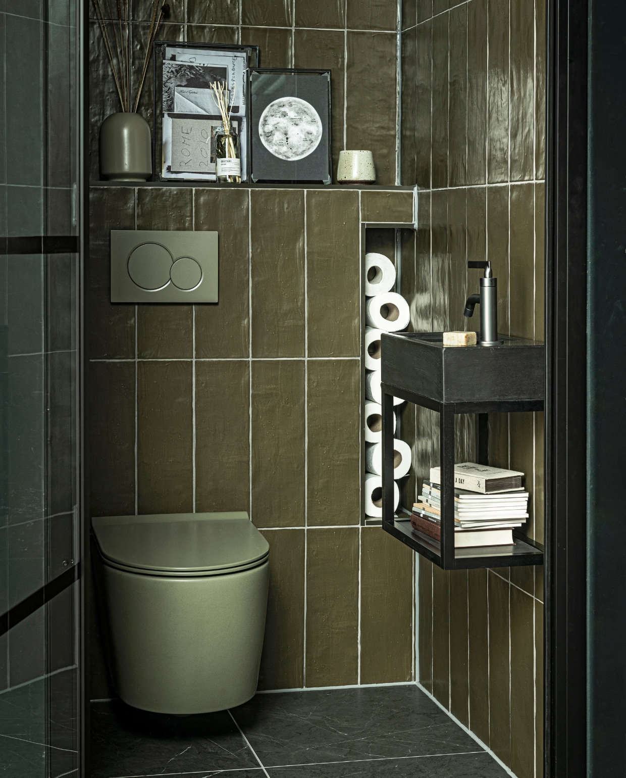 Fontein Tank in kleur Concrete Black, 40x22x10 cm(bxdxh) € 299,- (ook in Concrete en in White, hoogte 5,5 cm), metalen onderstel Fontein Frame in Zwart, 40x22x30 cm (bxdxh) € 339,-, hendel wastafelkraan Grip in kleur Black Steel € 459,- (ook in Charcoal, Bronze,Brushed en Chrome en met twee hendels), wandtegelMediterranea in kleur mat Camouflage, 3,2×40 cmper m² € 61,75, vloertegel Classic Black mat, 74×74 cmper m² € 73,05 (ook in 74×148, 30×60 en 7,3×30 cm).M.m.v. tegeldepot (toilet), ikea.nl (vaas), vtwonen.nl (fotolijsten). vtwonen collectie 08-2020 badkamer | styling Kim van Rossenberg | fotografie Sjoerd Eickmans