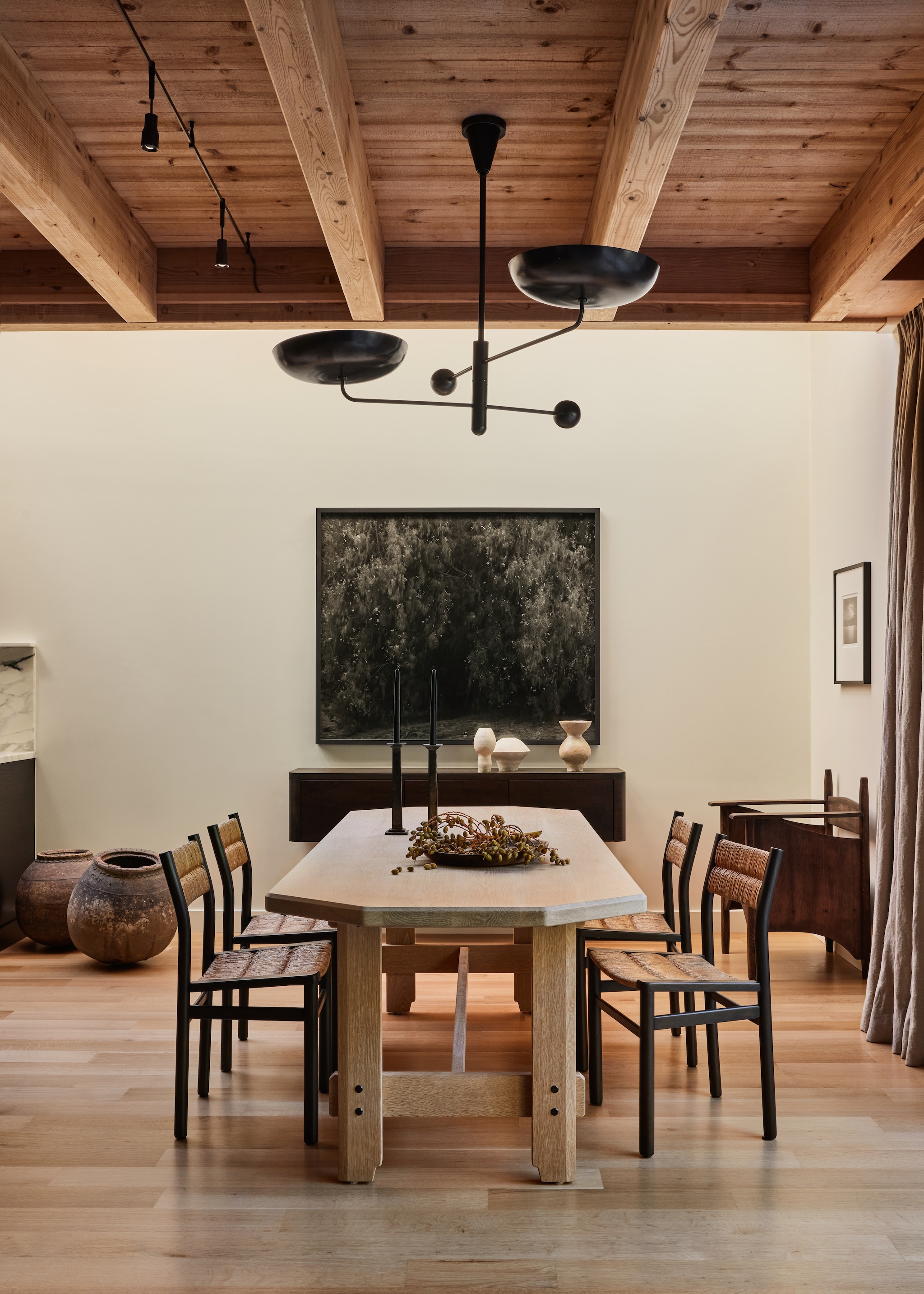 Vintage Franse eetkamerstoelen, soortgelijke Charlotte Perriand voor Robert Sentou. Antieke potten en antieke stoel rechts Galerie Provenance. Handgemaakte houten eettafel Rw Guild. Maatwerk dressoir naar eigen ontwerp. Hanglamp op maat Remains Lighting. Fotografiewerk Awoiska van der Molen. Linnen gordijn De Le Cuona, soortgelijke Libeco en By Mölle. Op de muur Afm Safecoat verf White Dove van Benjamin Moore.Op de tafel vondsten uit de natuur als decoratie.  vtwonen Landelijk 01-2026 | styling Kendra Smoot | fotografie Nicole Franzen