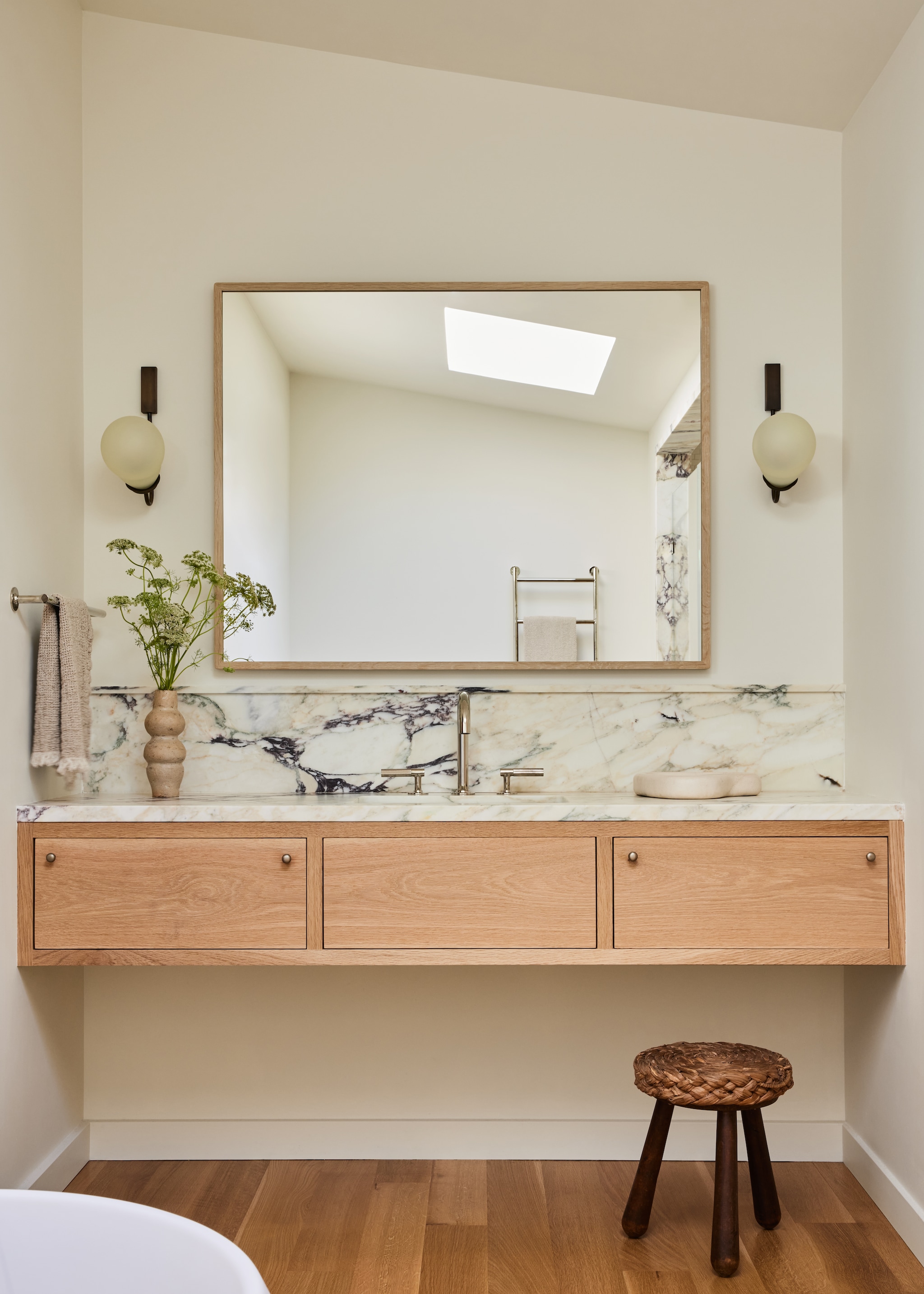 Maatwerk wastafelmeubel van marmer en eikenhout. Kranen Agape. Wandlampen Studio Giancarlo Valle. Antieke kruk Galerie Provenance. Massief houten vloer.  vtwonen Landelijk 01-2026 | styling Kendra Smoot | fotografie Nicole Franzen