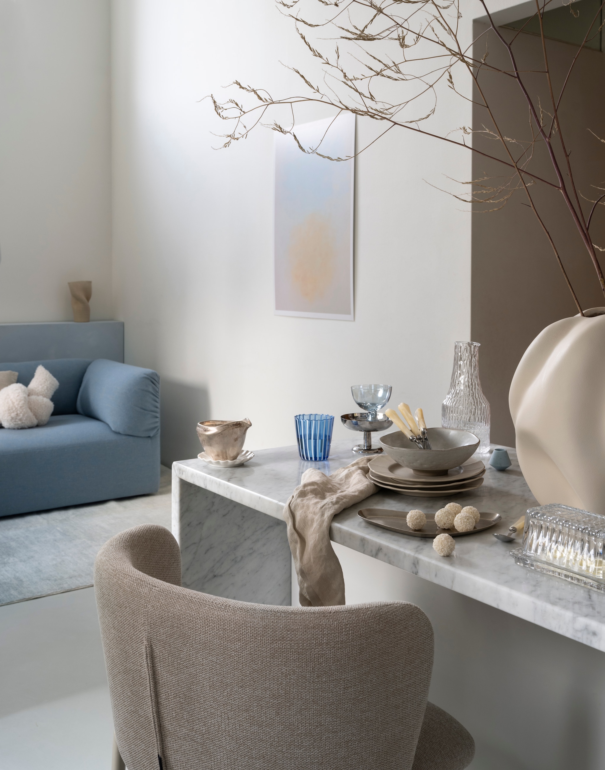 Studio Henk driezitsbank Unfold, stof hemp, Dale Hwp18, 220x90x70 cm (bxdxh) € 4000,- (studiohenk.nl). Kave Home barkruk Ciselia, stof en metaal, beige, 54x48x88,5 cm (bxdxh) € 229,- (kavehome.com). Arket ijscoupe, roestvrij staal € 22,- (arket.com). Pstr Studio poster Yesterday the beauty of the dawn, ontwerp Helen Butler, papier € 36,- (pstrstudio.com). Zara Home dessertbord met verhoogde rand, aardewerk, zand € 9,99, kom met verhoogde rand, aardewerk, zand € 9,99, bestekset met parelmoereffect handvat, pearl grey, 4-delig € 17,99, mok en schotel met gegolfde rand, porselein, wit € 7,99, botervloot, glas, gestreept € 15,99, glas, borosilicaat met strepen, blauw € 9,99, dessertcoupe, glas, blauw € 5,99 (zarahome.com). Søstrene grene servet, linnen, beige€ 3,99 (sostrenegrene.nl). H&m Home karaf, glas € 15,99 (hm.com). Kwantum kussen Knotty, polyester, offwhite € 10,-, vaas Melted, keramiek, beige € 19,-, vaas Isili, wit € 29,- (kwantum.nl). vtwonen 01-2026 | styling Sanne Ketelaar | fotografie Stan Koolen