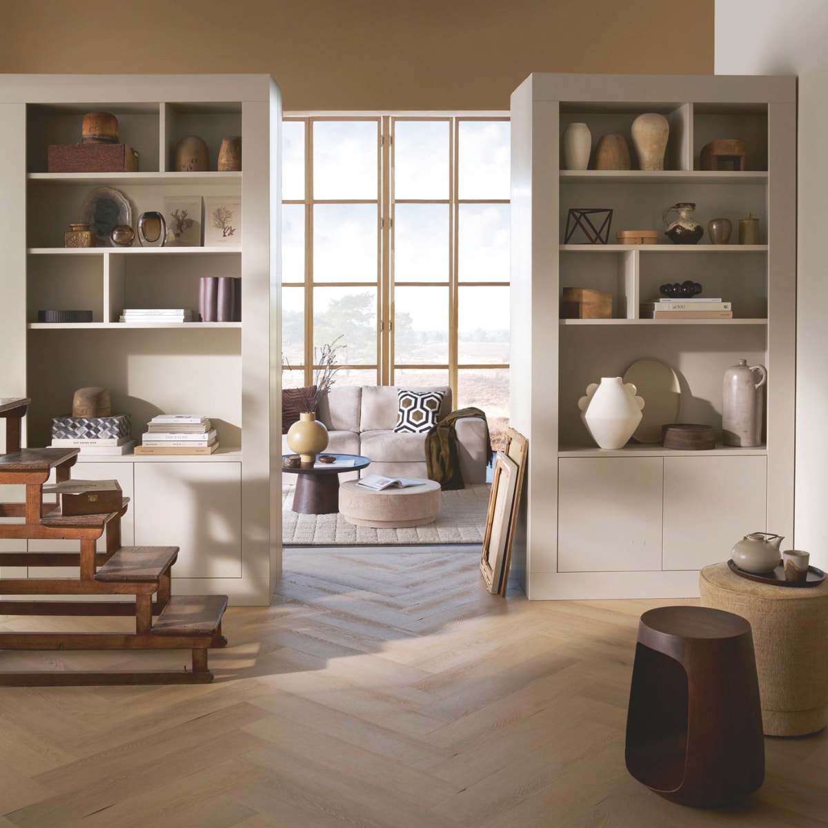 vtwonen wandkast Wallcover, grenen, dust, 117x31x229 cm (bxdxh), per stuk € 799,-, vtwonen poef Pearl en poef Pearl XL, melange stof, naturel, 40x45 cm (Øxh) € 199,- en 80x28 cm (Øxh)€ 199,-, vtwonen salontafel Coffee A Gogo, mangohout, walnoot, 90x40 cm (Øxh) € 499,- en vtwonen 2,5-zitselementenbank Family, geweven stof, zand, 298x98x85 cm (bxdxh) € 1999,-.M.m.v. pietjonker.nl (bibliotheektrap, bijzettafel), hm.com (grafisch kussen), weldaad.com (servies, opbergmand, linnen kussens), burbriantiek.nl (kruiken), vtwonen.nl (visgraat laminaat Rafter, vloerkleed Blocks). Overig privébezit.