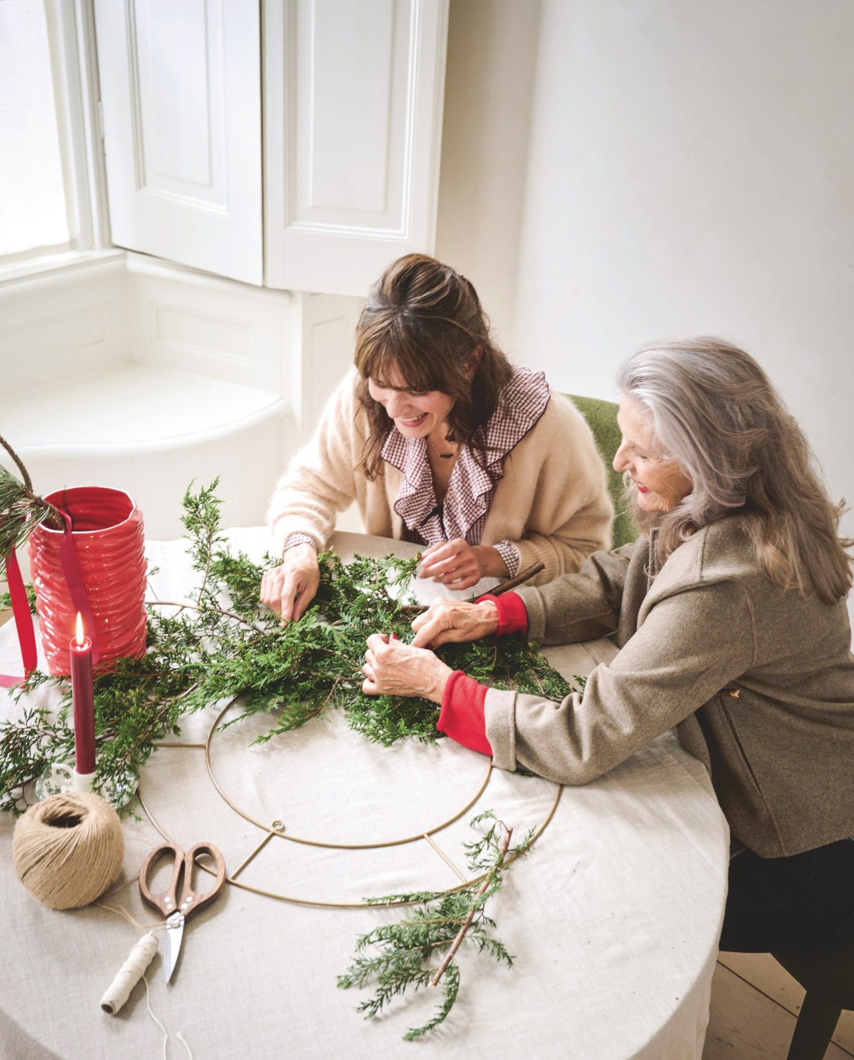 Zara Home tafelkleed, linnen € 69,99, vaas geribbeld, porselein, rood € 49,99, kandelaar, porselein € 11,99, schaar, hout € 29,99 (zarahome.com). vtwonen decoratiering, goud, 60 cm (Ø) € 29,50 (shop.vtwonen.nl). Overig privébezit. Kleding Helena (moeder): Bellerose vest (orangebag.nl). Zara geruite top (zara.com). Massimo Dutti jeans (massimodutti.com). Kleding Willemijn (oma): Massimo Dutti jasje, top, jeans (massimodutti.com). vtwonen kerstspecial 2025 | styling Danielle Verheul | fotografie Sjoerd Eickmans