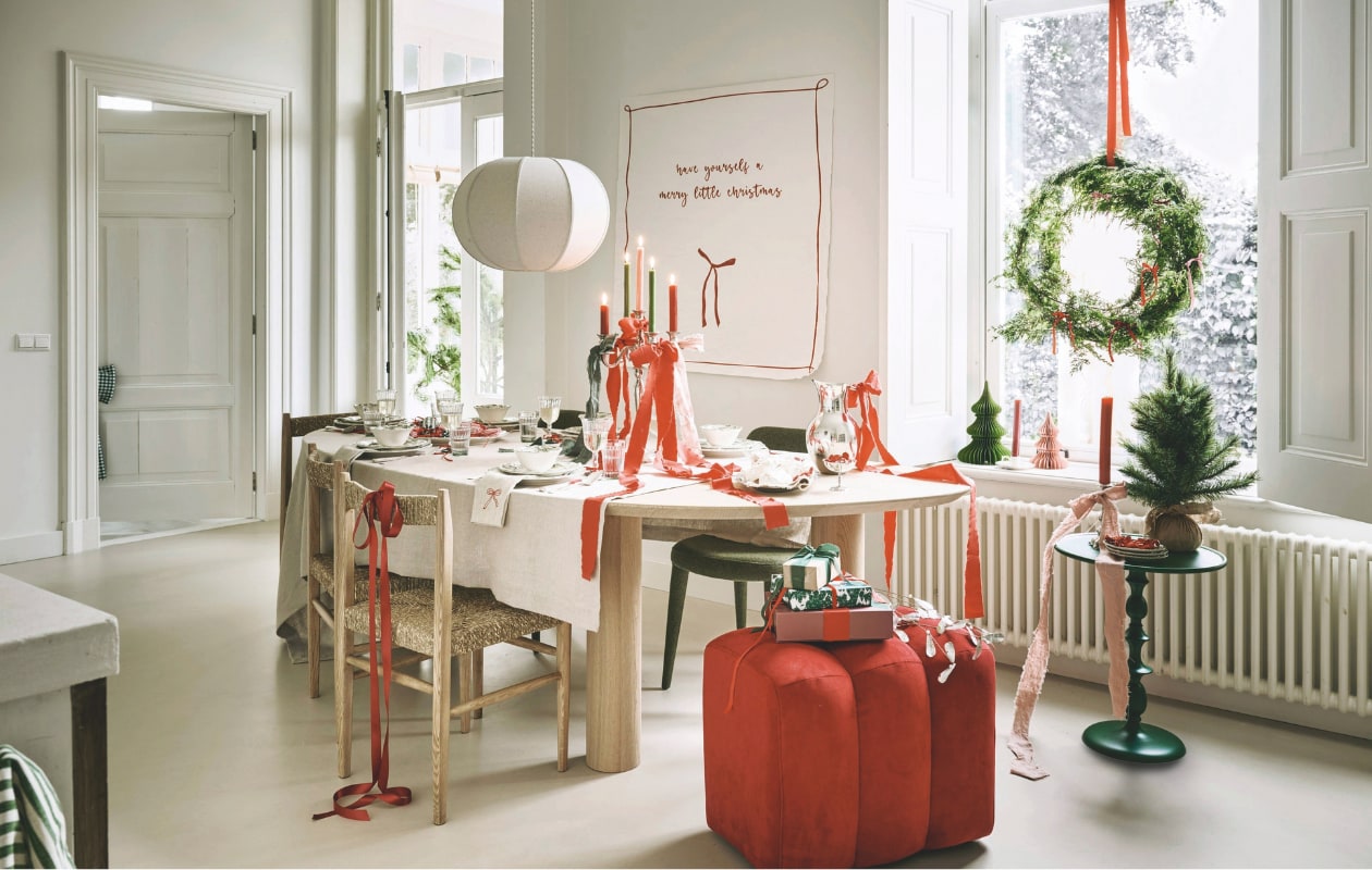 Firma Hout en Staal eettafel, eikenhout, 250x110x76 cm (lxbxh) vanaf € 1728,-, poef, rood € 250,- (loods5.nl). Zara Home stoel, essenhout en zeegras, 43x43x82 cm (bxdxh) € 189,-, hanglamp, katoen, wit, 48x24,5 cm (Øxh) € 79,99, servies, porselein, groen, per stuk vanaf € 6,99, waterglazen € 3,99, wijnglazen € 3,99, tafelkleed, linnen € 69,99, kandelaar, porselein, groen € 11,99 (zarahome.com). Polspotten eetkamerstoel Cosy, forest green, € 400,-, bijzettafel Classic, metaal, groen € 260,- (polspotten.com). Kulu Club servetten, linnen met geborduurde strik, set van 2 € 23,95. The Green Home Company kerstboom met kluit € 26,95, Urban Nature Culture schaal op pootjes, hout € 34,99. vtwonen ring met krans € 29,95 (shop.vtwonen.nl).  Tableware Amsterdam bestek, antiek, zilver, per couvert € 45,-, kandelaar, verzilverd € 75,-, dienblad, verzilverd € 20,-, coupe, rvs € 12,50 (tableware.amsterdam). H&m karaf, rvs € 39,99, theedoek, groen-wit € 4,99 (hm.com). Mo-ca home poster, canvas, eigen ontwerp gedrukt, vanaf € 16,95 (mo-cahome.com).Bungalow kerstornamenten, bomen, papier, groen en roze, per stuk vanaf € 10,-, mistletoe, metaal € 47,50 (bungalow.dk). Søstrene Grene geschenkdoos, papier, rood-roze € 4,18 (sostrenegrene.com). Overig privébezit. vtwonen kerstspecial 2025 | styling Danielle Verheul | fotografie Sjoerd Eickmans