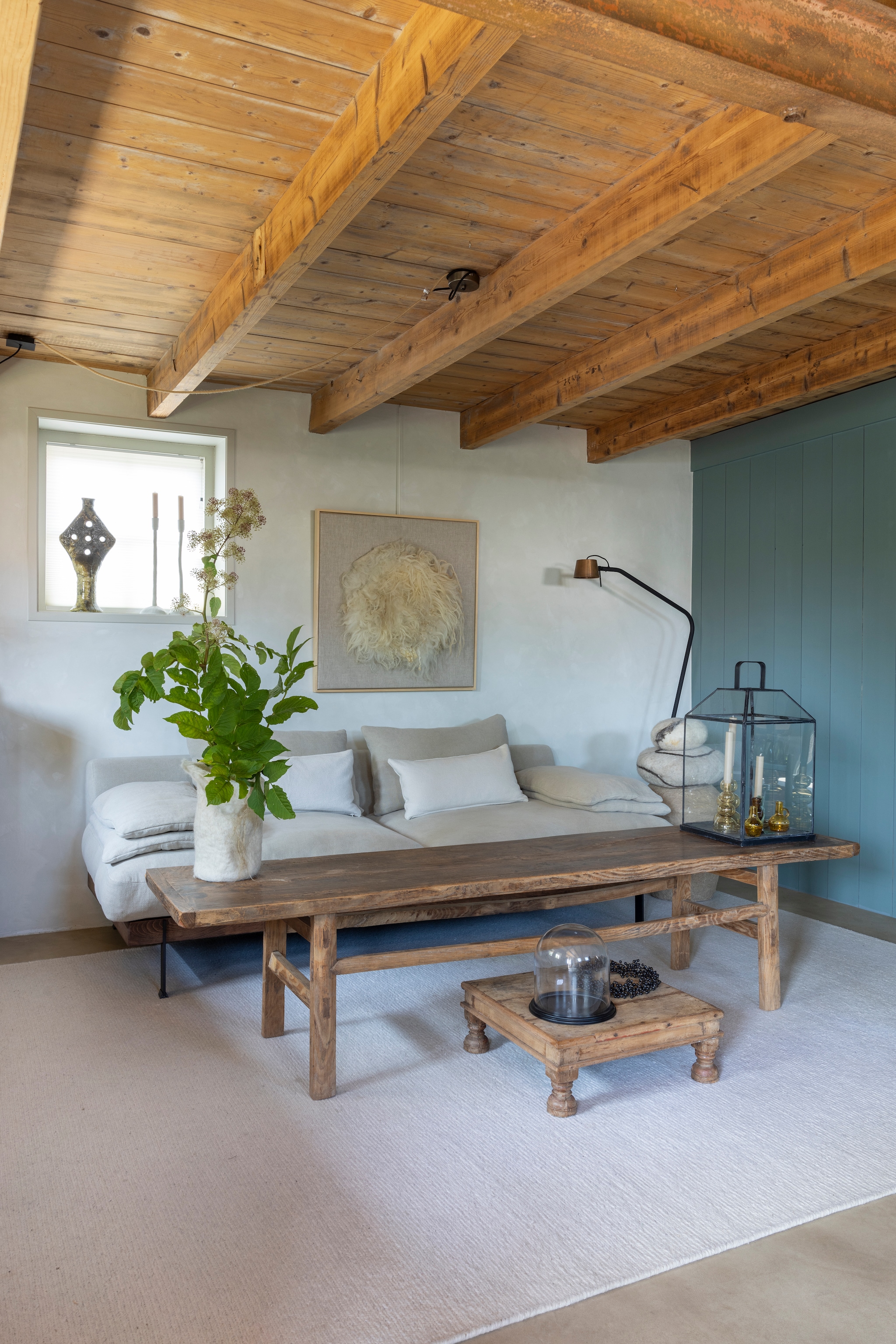 Houten wand kleur Blue Reef van Pure & Original. Stucco wand kleur Krijt en kozijnen kleur Tuinkamer van l’Authentique. Bank Ciel van l’Authentique. Kussens Ml Fabrics. Tafels Aura Peeperkorn. Staande lamp Frezoli Lighting. Lantaarn Chic Antique. Vloerkleed, items in de lantaarn en kandelaars op vensterbank Zv Wonen. Vaas, keien en kunstwerk Zilt & Zacht. Vaas papier-maché J-line. vtwonen Landelijk 02-2026 | fotografie Anneke Gambon