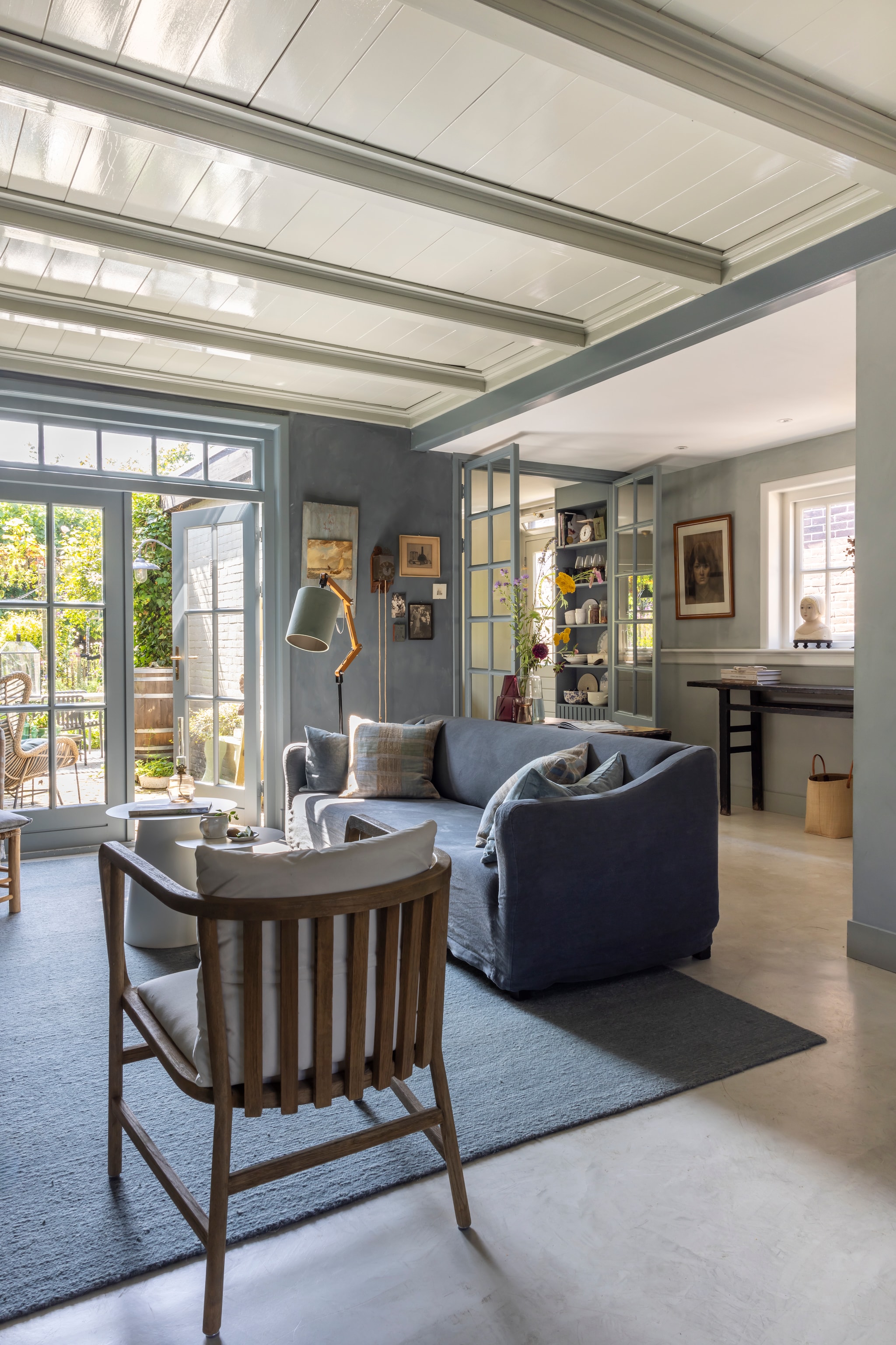 Vloerkleed Zv Wonen. Bank Gijs van l’Authentique. Bijzettafels en hoge sidetable Netty de Groot. Kussens Ml Fabrics. Lamp Hübsch. Stoel Leeff. Klok veiling Haarlem. Buste op vensterbank Meander. Kunst aan de muur Bert Schaap. Vloer beton ciré. Muurkleuren Blue Stone en Silverplate van Pure & Original. vtwonen Landelijk 02-2026 | fotografie Anneke Gambon