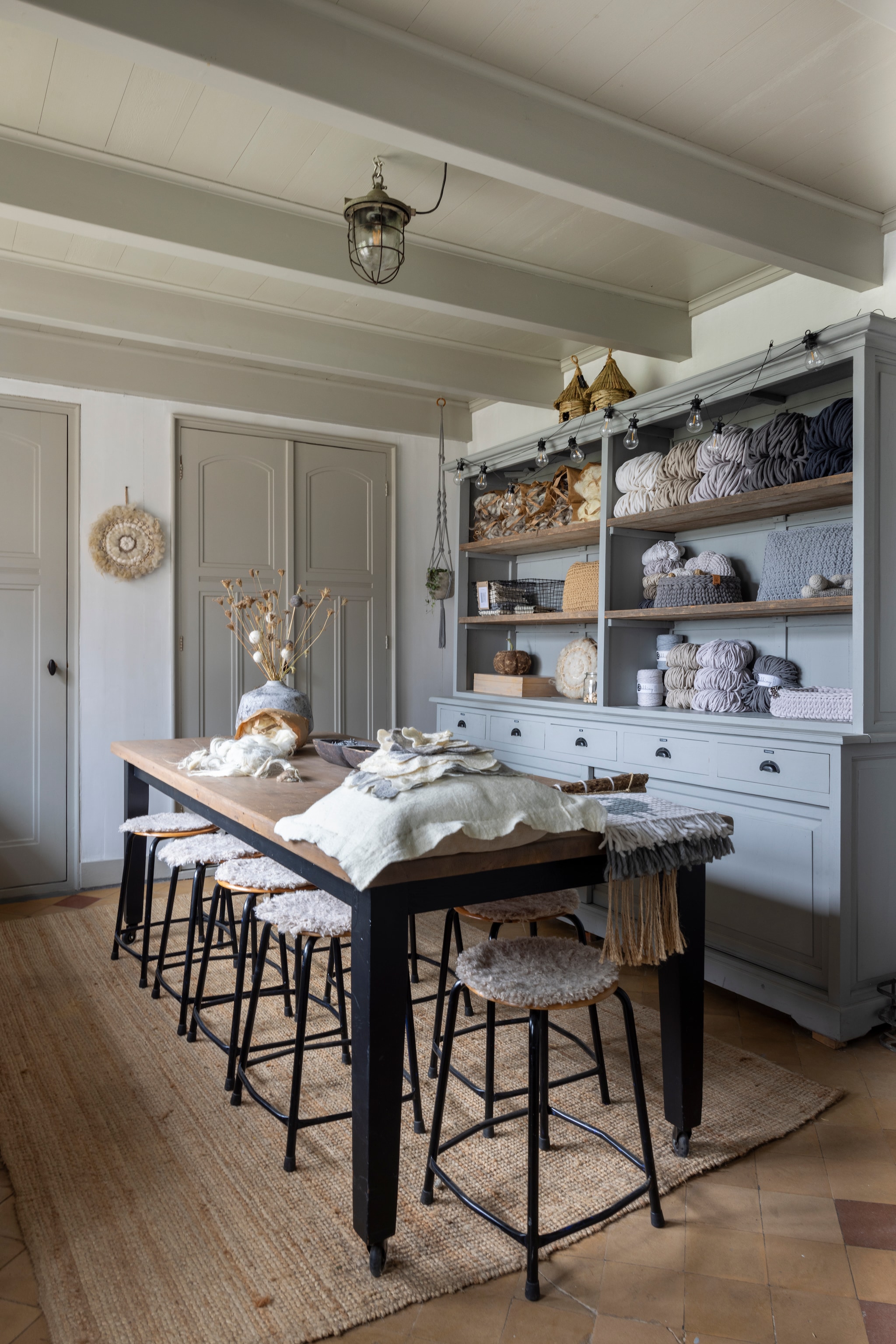 Workshopruimte van wolatelier WenKR8. Tafel cadeau. Pottenbakkers-krukken Marktplaats. Vachten erop en vloerkleed Ikea. Kleur kast Slate van Painting the Past. vtwonen Landelijk 02-2026 | fotografie Anneke Gambon