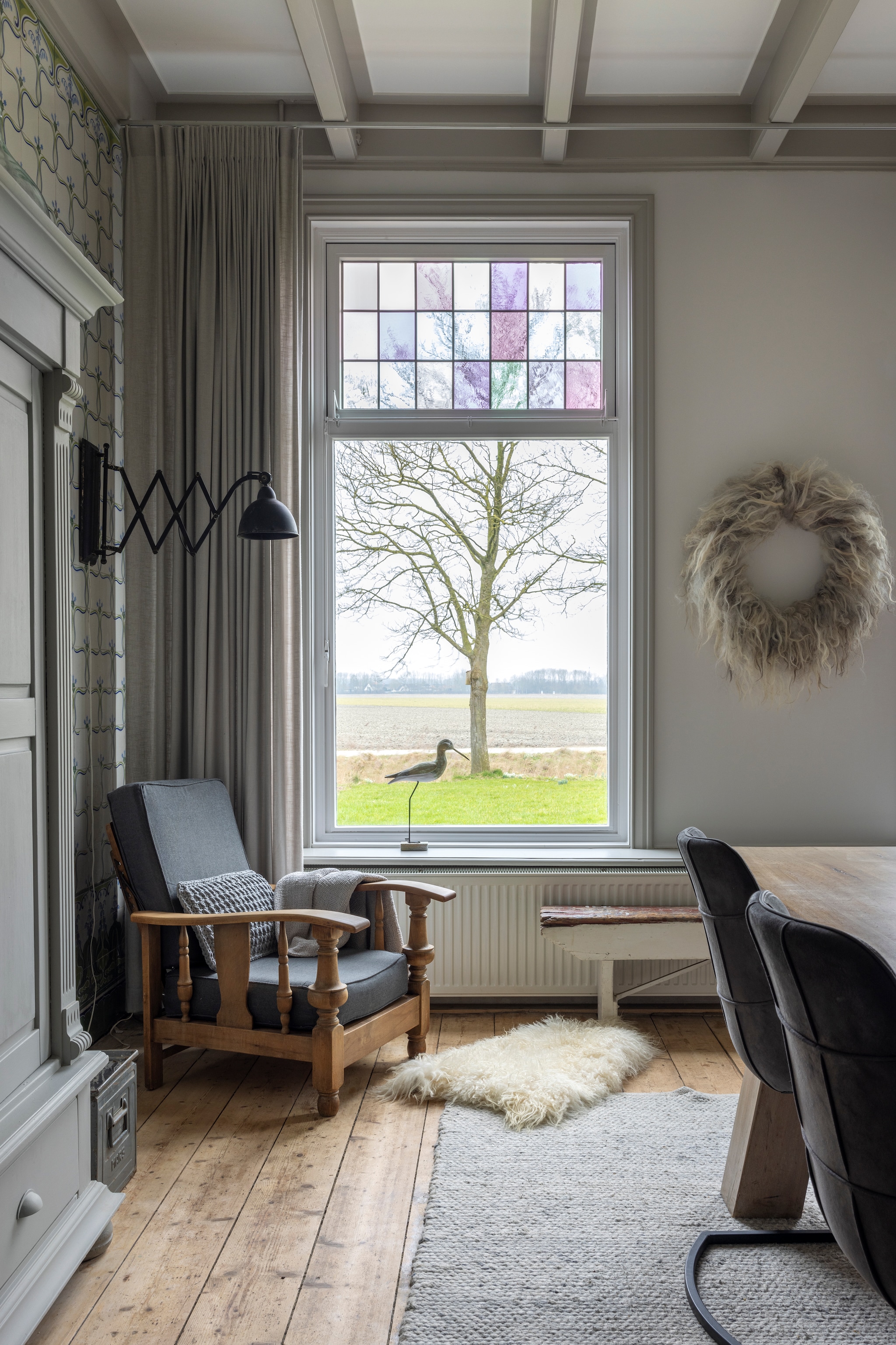 Grijze kast, fauteuil en wandlamp Marktplaats. Loesanne verfde de kast en stoffeerde de fauteuil. Kussen in de stoel en krans WenKR8. Vacht Van Buren Bolsward. Bankje onder raam gevonden in de schuur. Gordijnen Colors@Home Dijkstra. vtwonen Landelijk 02-2026 | fotografie Anneke Gambon