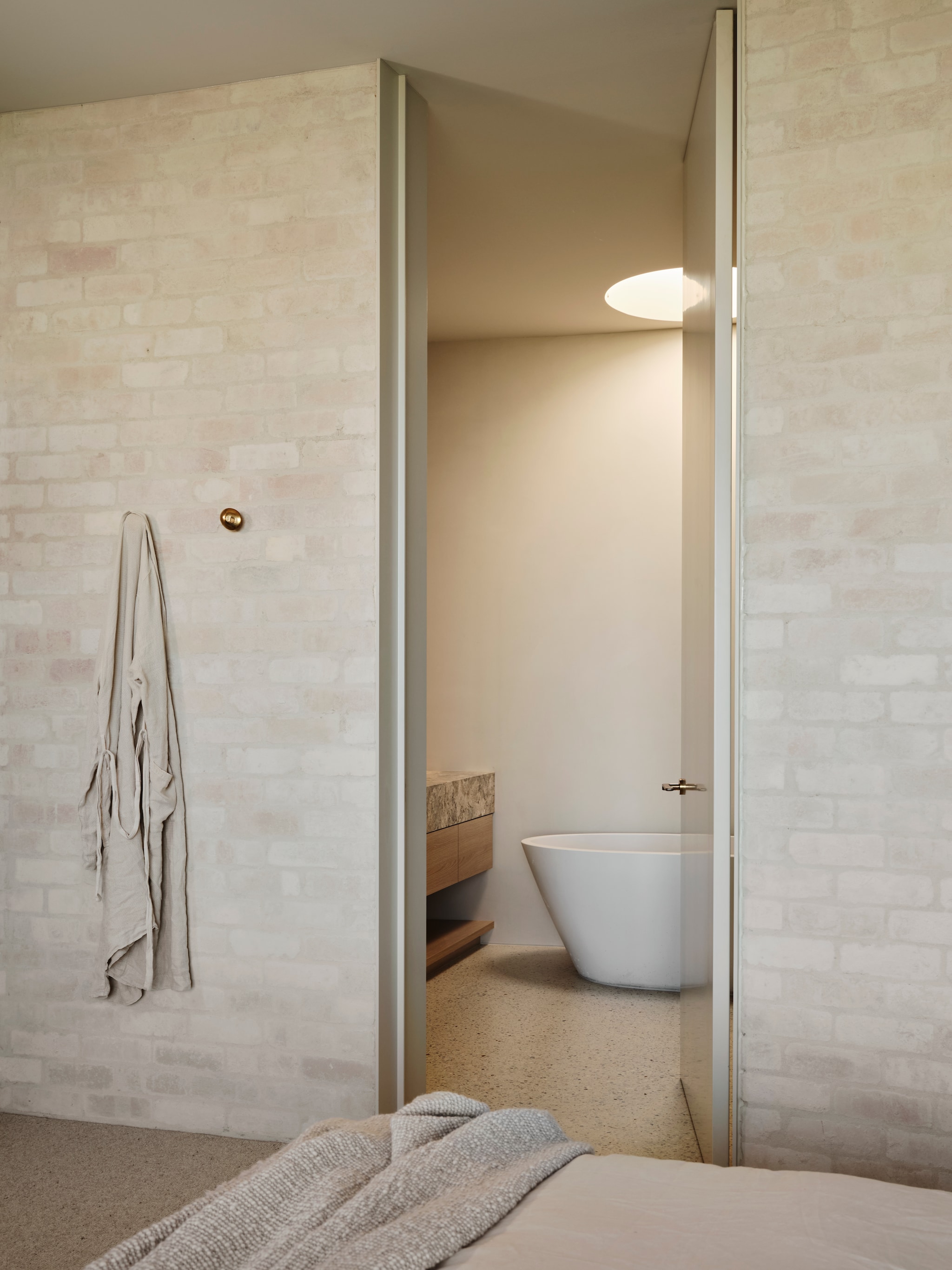 Badkamer met betonnen bad Nood Australia. Op maat ontworpen wastafelmeubel van eikenhout en travertin. vtwonen Design 01-2026 | productie Living Inside | fotografie Lisa Cohen