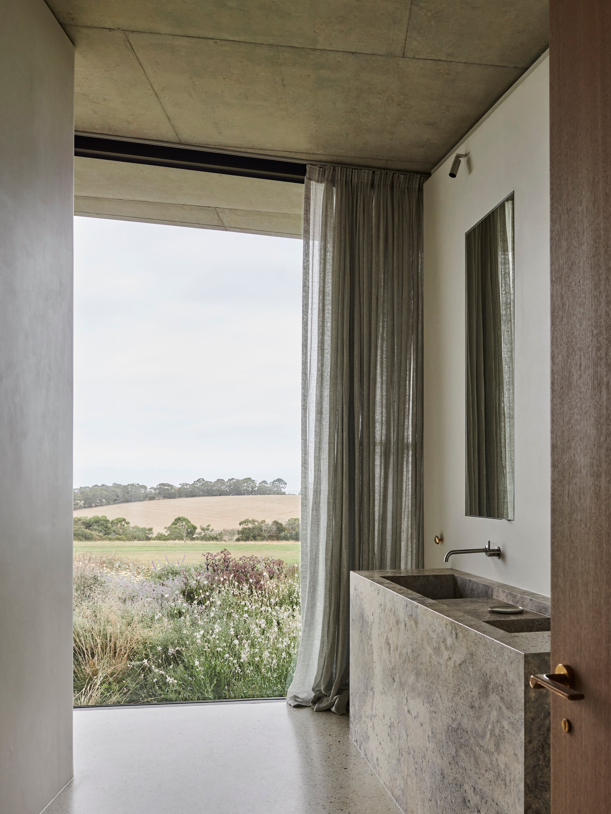 Op maat gemaakte wastafel in zilver travertin. Kranen Brodware. Gordijnen van linnen. vtwonen Design 01-2026 | productie Living Inside | fotografie Lisa Cohen