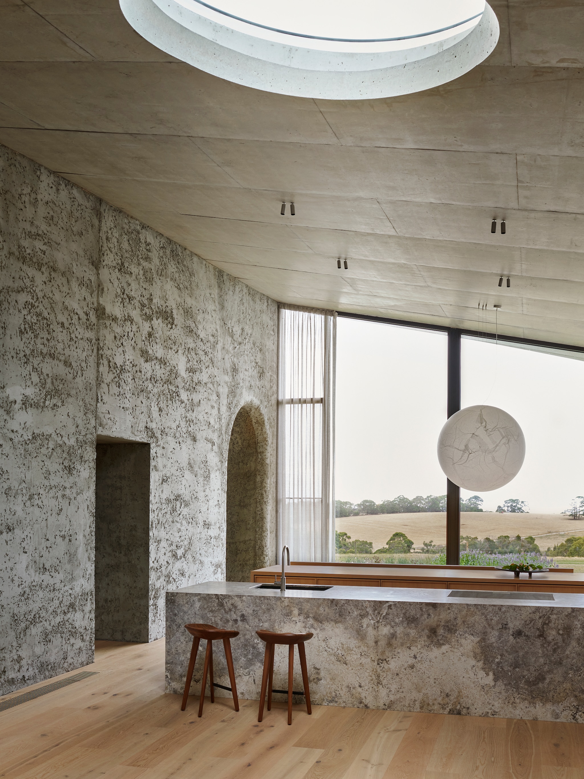 Op maat gemaakte keuken van massief eiken en travertin. Krukken Bassamfellows. Lamp Davide Groppi. vtwonen Design 01-2026 | Productie Living Inside | Fotografie Lisa Cohen