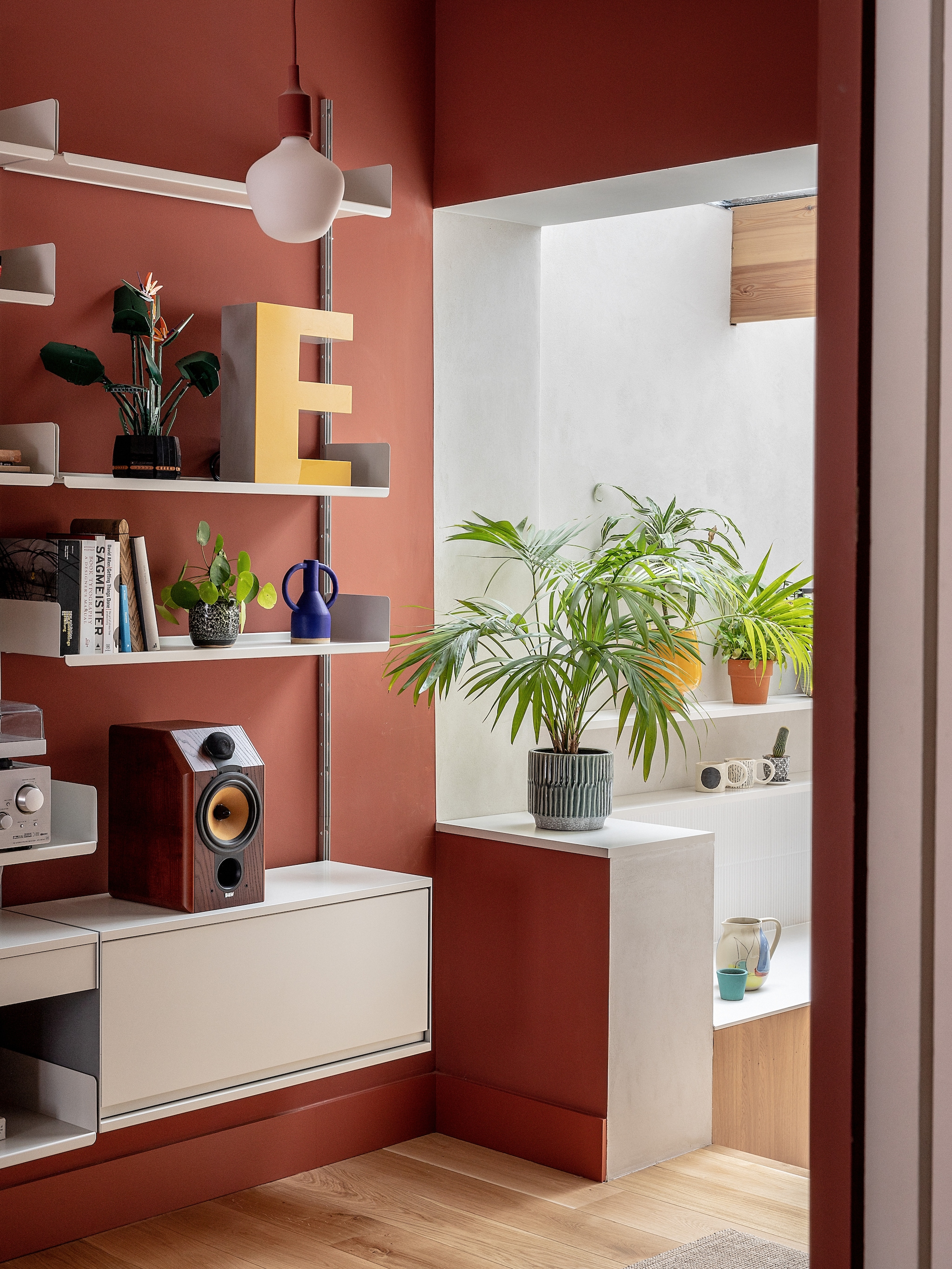 Muren in Red 01 van Lick. Rode hanglamp Muuto. Wall unit 606 van Vitsoe. Eikenhouten vloer Havwoods. Vintage speakers Bowers&Wilkins. Draaitafel Pro-Ject. Versterker Sony. Lamp letter E vintage. vtwonen 02-2026 | fotografie Taran Wilkhu | productie Living Inside