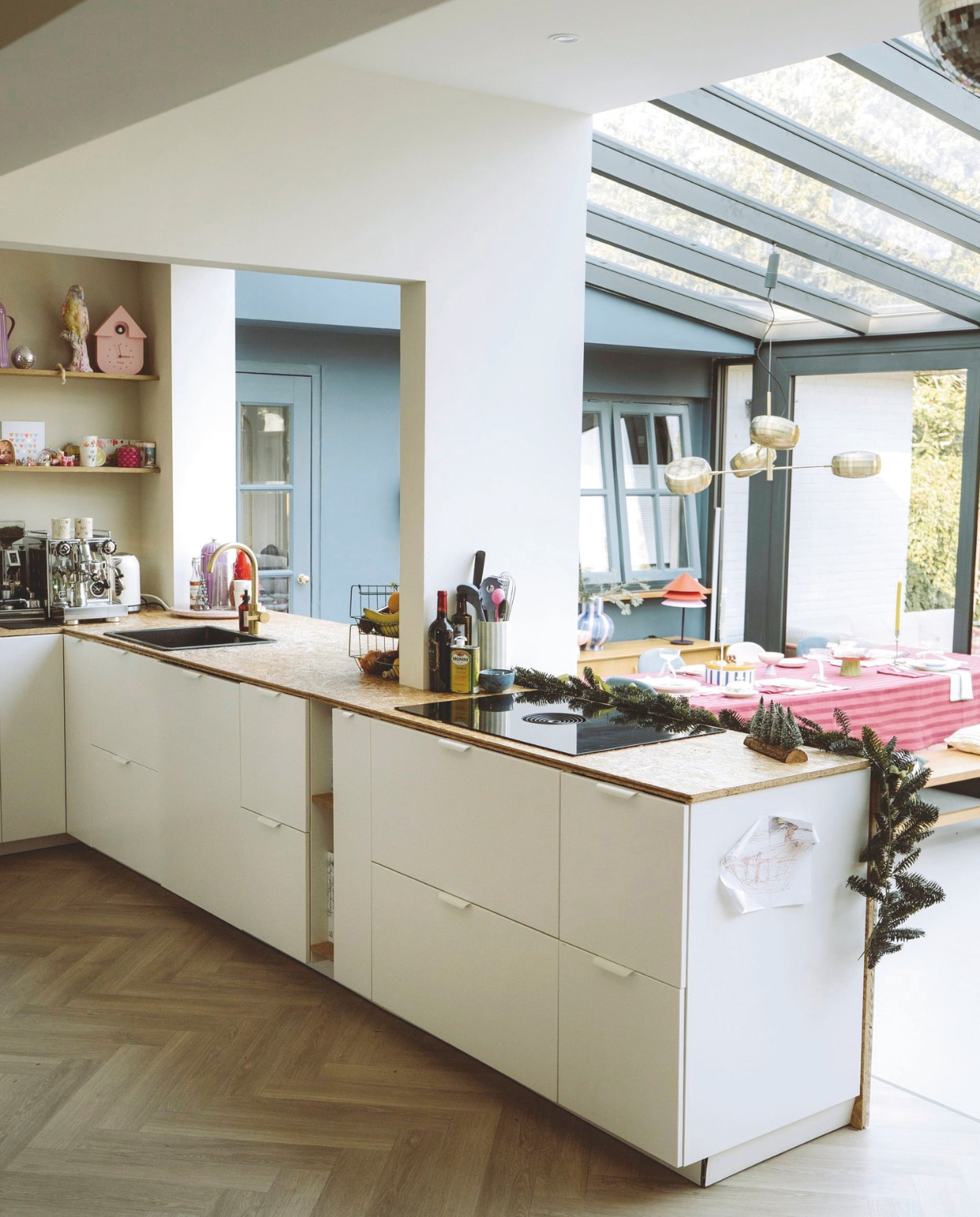 Keuken Ikea met blad van osb-plaat. Kraan Ikea. Koffiemachine Rocket. Kopjes zelfgemaakt. Klok Karlsson. Theekan Rice. Fruitrek souvenir uit Denemarken. Lamp Zuiver. Kleur uitbouw Denim van Painting the Past. Bankje Ikea. Kussens Karwei. Stoel Kwantum. vtwonen 11-2025 | styling Sanne Ketelaar | fotografie Stories By Chriske  | tekst Merel van der Lande