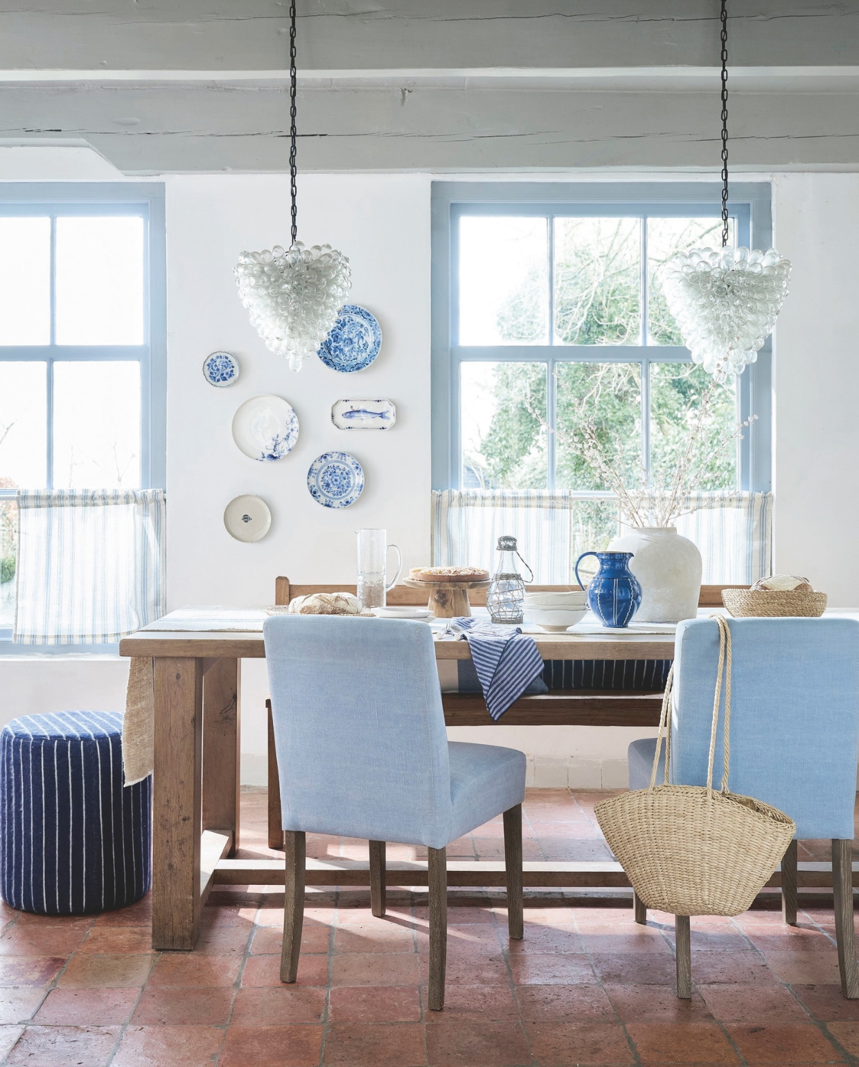 Eikenhouten eettafel van Gebr. De Ruiter, prijs op aanvraag (oudeikentafels.nl). Tafelkleed van graanzakken, per strekkende meter € 29,95 (vandijkenko.nl). Gestoffeerde eetkamerstoel Iris € 225,-, handgemaakt rieten bord € 19,95 (hetkabinet.nl). Wollen poef Pinstripe Midnight, 45x50 cm (Øxh) € 179,- (thesouks.nl). Linnen bistrogordijnen, 65x60 cm (bxh), set van 2 € 60,- (bol.com). Glazen kan Hammered € 39,95, zeegras mand Corn, set van 2 € 24,95 en houten schaaltjes Pesce € 9,95 van Urban Nature Culture (shop.vtwonen.nl). Gebaksbord met zeemotief (aan de wand) € 12,-, glazen fles met rotan dop € 22,99, aardewerken vaas € 89,99, aardewerken kom met structuur € 11,99, blauwe aardewerken kan € 39,99, gestreept linnen servet, set van 2 € 15,99(zarahome.com). Houten taartplateau € 24,95 (dille-kamille.nl). Handgeblazen glazen hanglampen Vintage XL Grape 1960 van L’Artigiani (marktplaats.nl of reliving.nl). Vergelijkbare oude houten eettafelbank (hetjagershuis.com). Overig privébezit. vtwonen Landelijk 04-2025 | styling Kim van Rossenberg | fotografie Sjoerd Eickmans