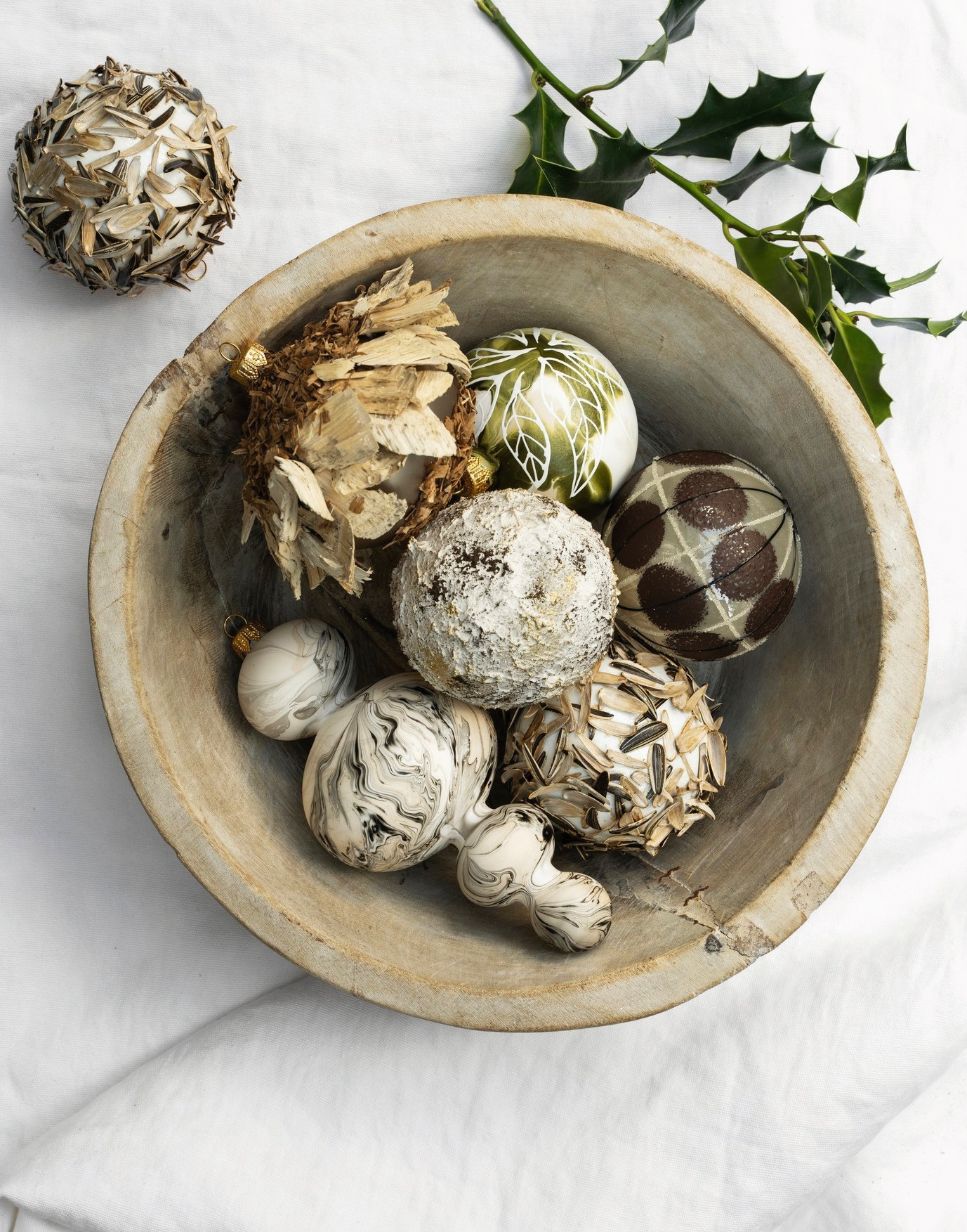 ’t Achterhuis schaal, hout, bruin € 60,- (achterhuis.nl). Dagmara kerstdecoratie mat gemarmerd, glas, zwart-wit € 15,90, kerstbal met zonnebloempitten, glas, naturel, set van 2 € 13,90, kerstbal met wit bladmotief, glas, olijfgroen, set van 2 € 19,90, kerstbal met stippen, glas, grijs-bruin € 19,90, kerstbal met ruwe textuur, glas, naturel, set van 2 € 19,90, kerstbal met houtkrullen, glas, beige, set van 2 € 21,90 (shop.vtwonen.nl). vtwonen landelijk 11-2025 | styling Marianne Luning | fotografie Stan Koolen