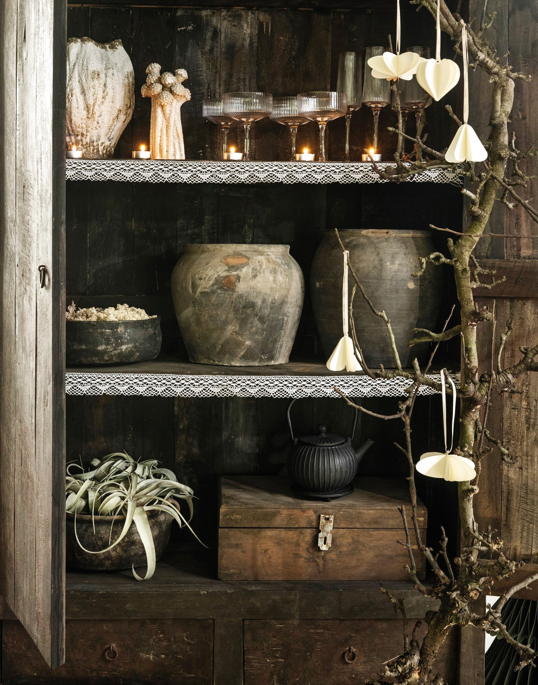 Aura Peeperkorn kast, oud teak, 112x50x190 cm (bxdxh) € 1695,-, potten, aardewerk, bruin € 89,90, potten, ijzer, bruin € 109,95, kist, hout, bruin € 129,95 (aurapeeperkorn.nl). Blomus kerstornament Kazary, papier, moonbeam, set van 4 € 24,95 (blomus.nl). Nordal vaas Henry S, keramiek, naturel € 90,91, kaarsenhouder Funghi, keramiek, gebroken wit € 40,15 (nordal.com). My Flowers.shop rendiermos, groen, per bak € 6,99, vtwonen champagneglazen, glas met gouden rand, set van 4 € 35,-,  (shop.vtwonen.nl). Dille & Kamille theepot, gietijzer, zwart € 59,95,- (dille-kamille.nl). De Boerenbonthal kant, wit, per rolletje € 5,95 (deboerenbonthal.nl). Olijfboomtak en planten privébezit. vtwonen landelijk 11-2025 | styling Marianne Luning | fotografie Stan Koolen