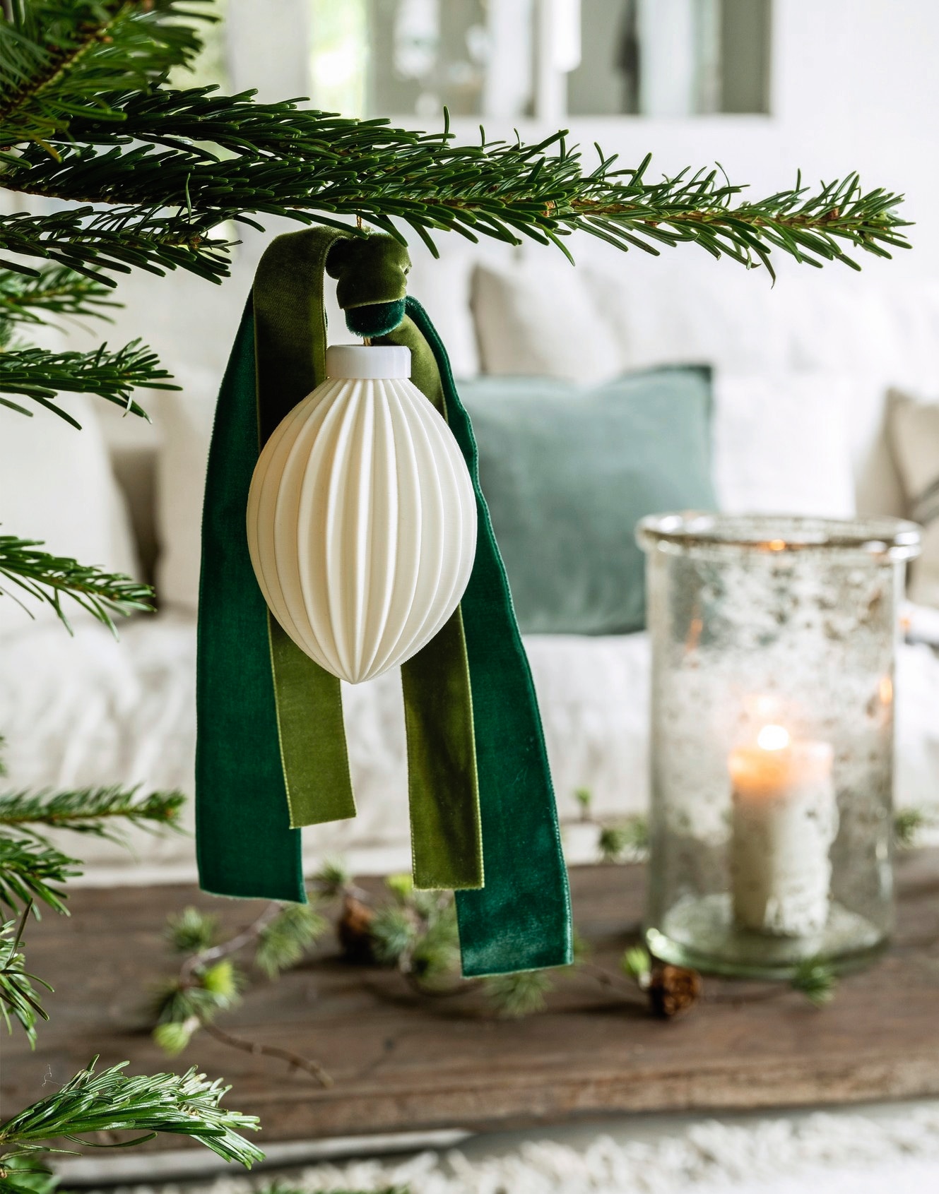 Aura Peeperkorn windlichten, glas € 89,95 (aurapeeperkorn.com). Madam Stoltz kussensloop, katoen en fluweel, groen € 29,75 (deens.nl). vtwonen kerstornament Stripes, porselein, wit € 8,95 (shop.vtwonen.nl). De Boerenbonthal lint, fluweel, groen, per meter vanaf € 2,50 (deboerenbonthal.nl). vtwonen landelijk 11-2025 | styling Marianne Luning | fotografie Stan Koolen