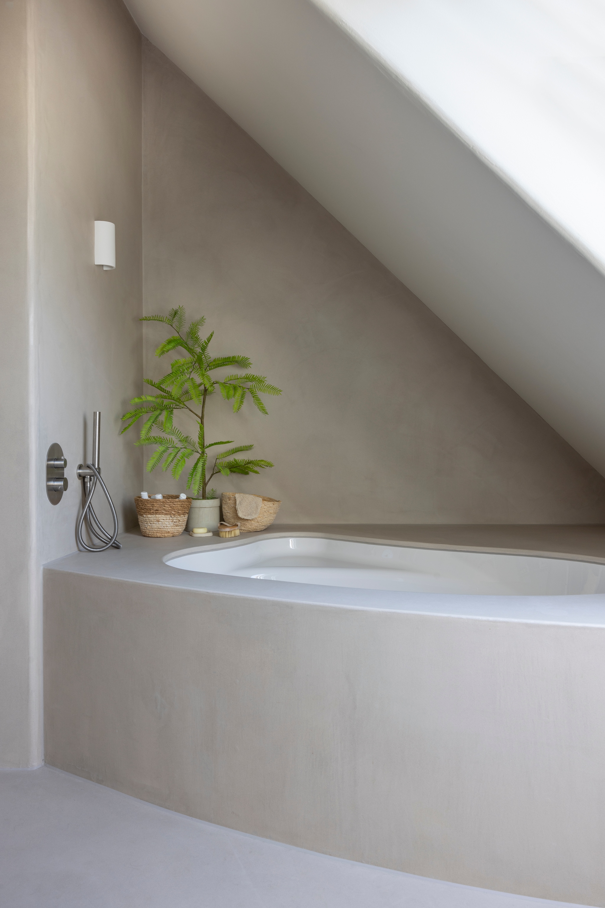 Wandlamp gips via Lampen24. Bad Lyra van Riho. Douchegarnituur van geborsteld rvs via Voordelig Design Sanitair. Badombouw eigen ontwerp en zelfgebouwd, afgewerkt met lavasteen. vtwonen Landelijk 03-2026 | fotografie Anneke Gambon