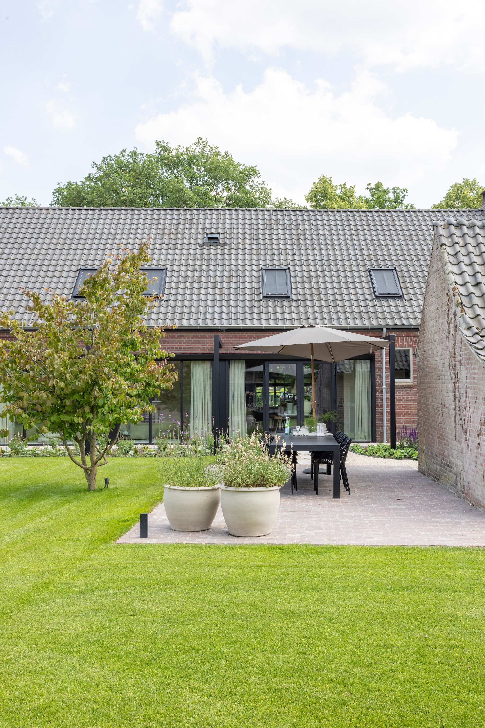 Potten geschilderd met muurverf. De stenen van het terras komen uit de boerderij. Soortgelijke parasol Home24. vtwonen Landelijk 03-2026 | fotografie Anneke Gambon
