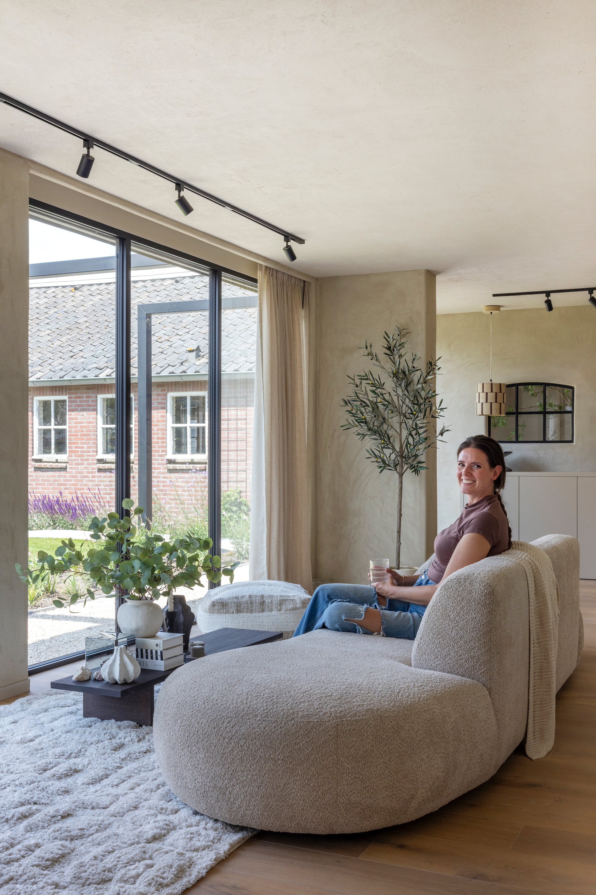 Bank Rozzano van Kwantum. Poef Coco homeliving. Salontafel Kona Display van Ferm Living. Vloerkleed Tibo van Benuta. Rail met spots Qub. Gordijnen Navajo 218440 van Raamstyling. Vloerplanken eiken 22 cm van Multiplank afgewerkt met hardwasolie 2K Harea 029. Stalraam via Marktplaats. Kunstboom eucalyptus via Rhodé Flowers. vtwonen Landelijk 03-2026 | fotografie Anneke Gambon