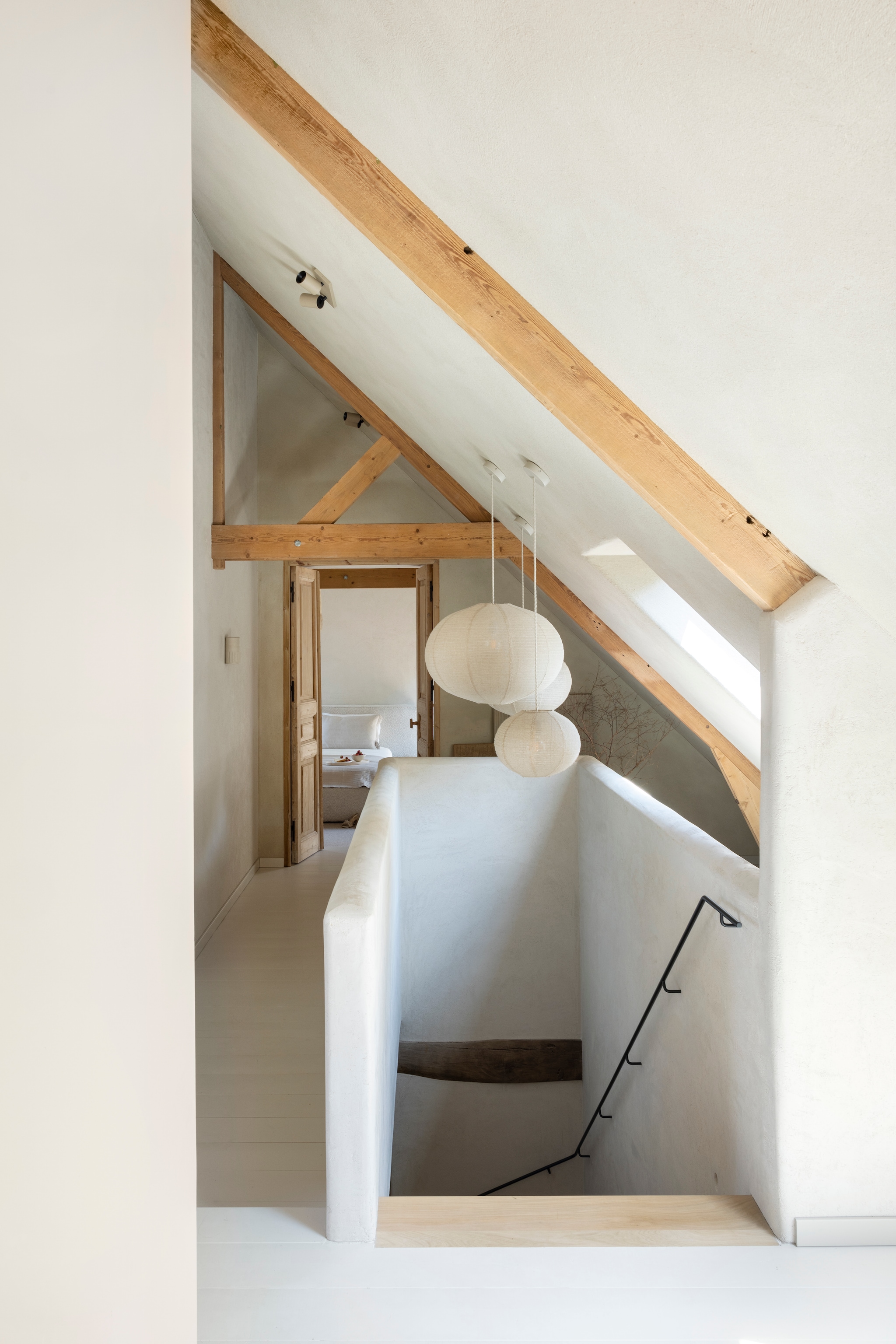 Hanglampen met linnen kap Zara Home. Spots Champagne van Mila. Trapleuning eigen ontwerp, uitgevoerd door Mitch Metaal. Wanden en balustrade witte basisleem met leem-finish met toegevoegd stro kleur Kolumba Grau van Yosima. De spanten zijn origineel en werden gezandstraald. vtwonen Landelijk 03-2026 | fotografie Anneke Gambon