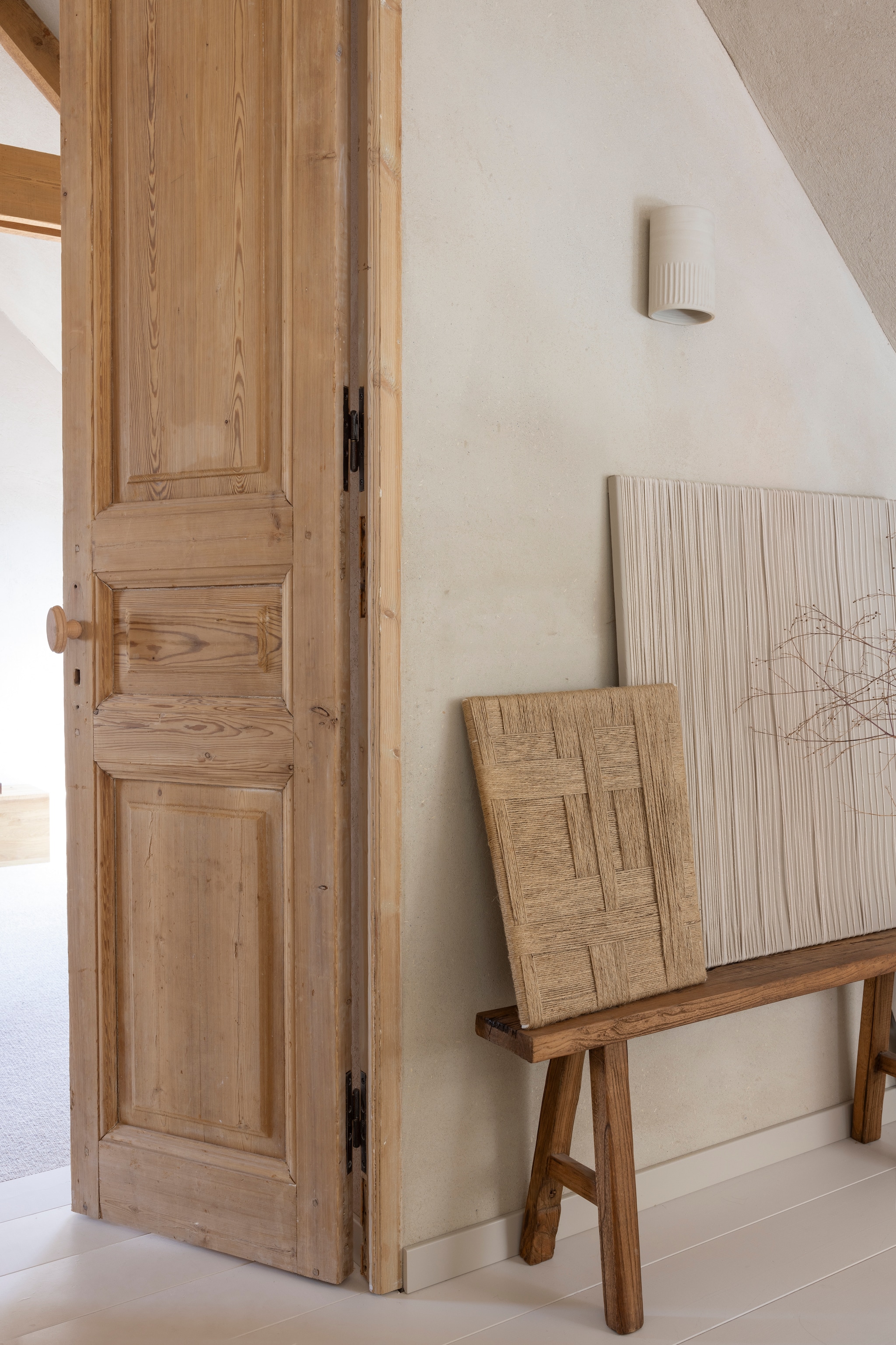 Wandlamp eigenontwerp, uitgevoerd door Atelier Ikigai. Deuren en kozijn Empire Best. Wanden witte basisleem met leemfinish met toegevoegd stro kleur Kolumba Grau van Yosima. Bankje Marktplaats. Kunstwerken zelfgemaakt. vtwonen Landelijk 03-2026 | fotografie Anneke Gambon