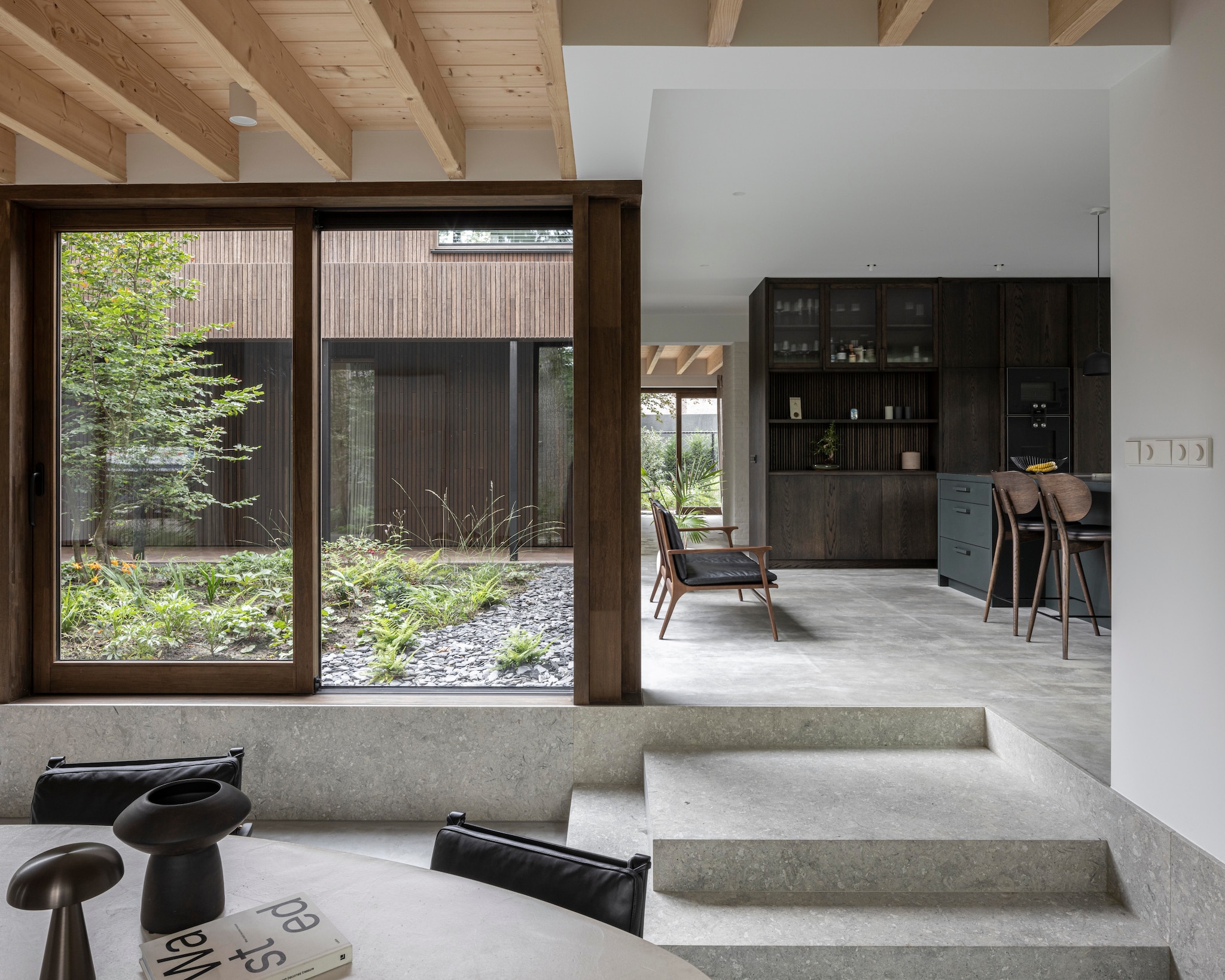 Stoelen Rén Dining Armchair van Stellar Works in eiken/zwart. Tafel Purdey D Design. Tafellampen &Tradition. Keukenstoelen Mater Design High Stool Backrest 69. De vloer is gemaakt van gevlinderd cement, de traptreden van Grigio Alpi-kalksteen.