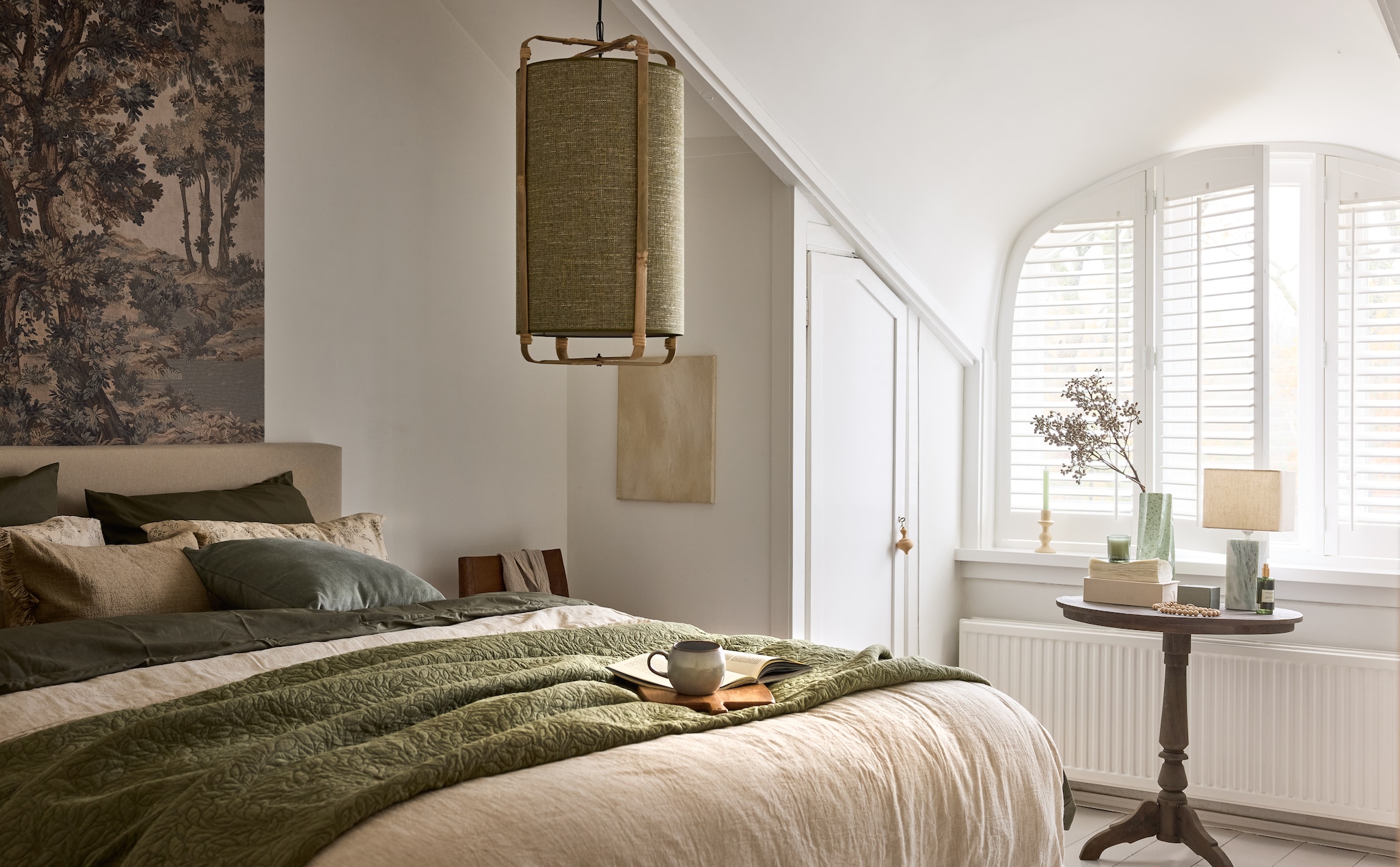 Raw Materials eetkamerstoel Freya, hout en leer, bruin, 50x45x80 cm (bxdxh) € 349,-, Light & Living hanglamp Sendai, stof en metaal, groen, 42 cm (Ø) € 199,95, Urban Nature Culture vaas Spille, keramiek, groen € 64,99 (shop.vtwonen.nl). Belartestudio behang Tapestry Landscape, beige, per m² € 55,- (belartestudio.com). Bonsoir kussen, fluweel, zachtgroen € 40,-, dekbedovertrek, katoensatijn, groen € 140,- (bonsoir.com). Zara Home dekbedovertrek, gestreepte structuur, katoen, gebroken wit € 119,-, bedsprei gewatteerd met bladeren, katoen, groen € 89,99, kussensloop bloemenprint, katoen, beige € 22,99, kussenhoes franjes, katoen, sand € 19,99, snijplank, hout, lichtbeige € 22,99, kamerjas, gewafeld linnen, beige € 119,- (zarahome.com). Schilderij, 30x40 cm (lxb), prijs op aanvraag (sanneketelaar.com). Dille & Kamille mok, steengoed, grijs € 8,50 (dille-kamille.nl). Overig privébezit. vtwonen Landelijk 02-2026 | styling Sanne Ketelaar | fotografie Alexander van Berge