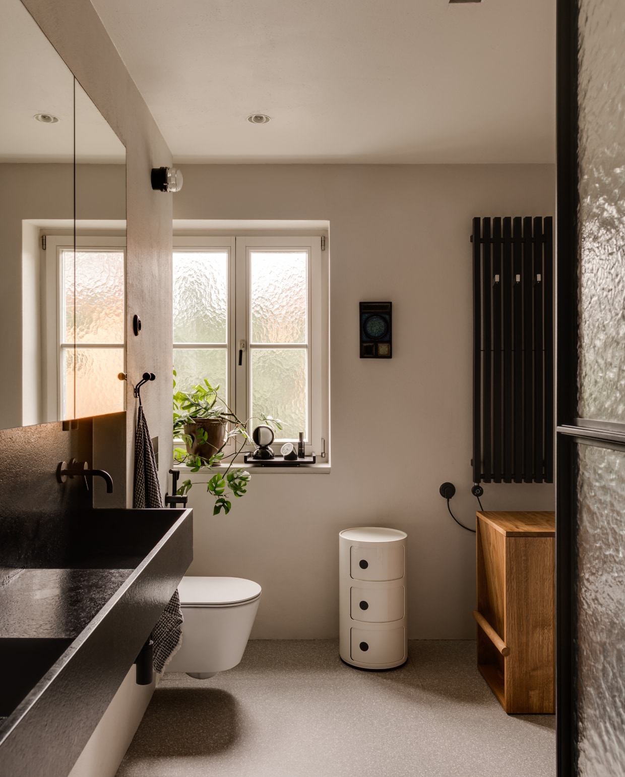 Vintage kast Componibili van Anna Castelli Ferrieri voor Kartell. Eiken ontwerp uniek stuk van Piotr Kuchciński. Wandlamp Fresnel 1148 van Joe Colombo voor Oluce. Op de vloer liggen terrazzo platen in een cementkleur. stijlvol wonen 10-2025 | fotografie oni studio