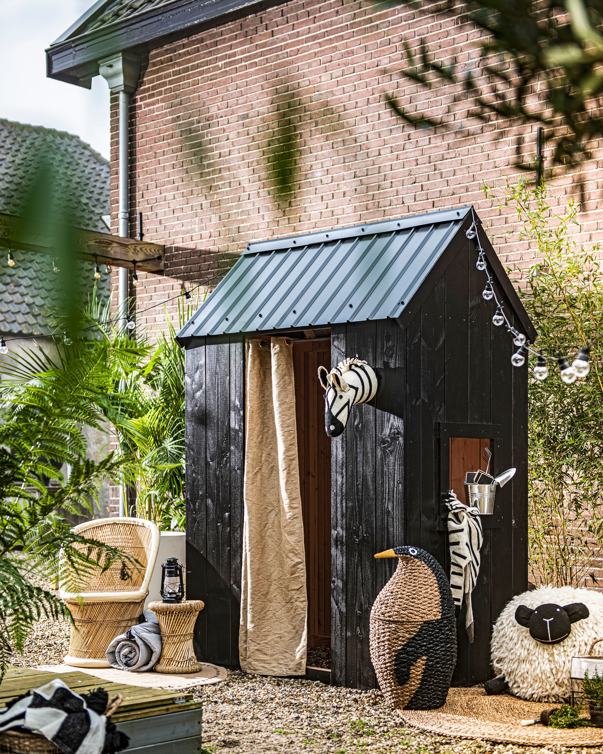 Lichtsnoer van Madam Stoltz, per stuk € 30,40, opgerold matras van Bloomingville € 54,99, zeegras vloerkleed van Bloomingville  € 94,90, opbergmand pinguïn van Bloomingville € 115,-, poef schaap van Bloomingville € 259,-, betonlook plantenpot van Ecopots Amsterdam, per stuk vanaf € 35,99, zeegras manden van Bloomingville, set van 2 € 56,60 (vtwonen.nl). Rotan stoel  € 45,-, rotan bijzettafel € 20,-  (vandijkenko.nl). Zwarte lantaarn  € 14,95, zinken plantenpot € 3,95, schep € 2,95, hark € 2,95, steeketiketten, per stuk € 1,25, glazen minikas € 19,95 (dille-kamille.nl). Rond vloerkleed met stippen € 34,99 (hm.com). Zebrakop € 25,-, zebravloerkleed € 30,- (loods5.nl). Zwart-wit gestreepte deken € 127,- (aaimadewitlove.com). Planten en bomen (greenlifestyle- store.nl). Verf Toms Oil Eggshell Buiten kleur Black Jack 119 (littlegreene.nl). Overig privébezit.   vtwonen special tuin 1 | ontwerp & uitvoering Johan Snoodijk | productie & styling Danielle Verheul | fotografie Sjoerd Eickmans | m.m.v. Little Green