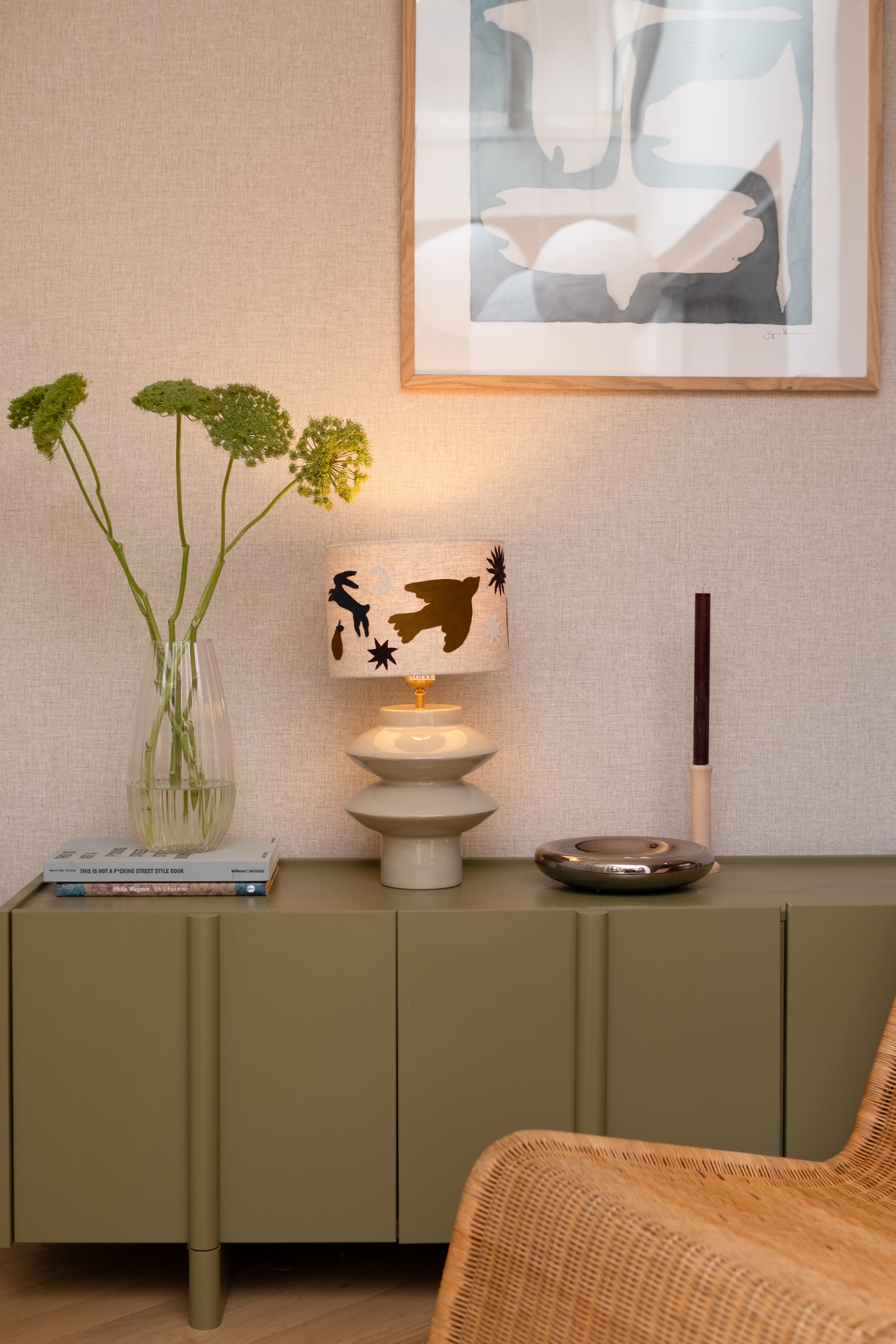 Lampenkap en lampvoet van Light & Living, poster van Pstr Store en dinerkaars van Bolsius via shop.vtwonen.nl. Glazen vaas en chromen schaal kringloop. Kandelaar Dille & Kamille. Dressoir Woood. Rieten fauteuil tweedehands. vtwonen 02-2026 | fotografie Valerie Paas