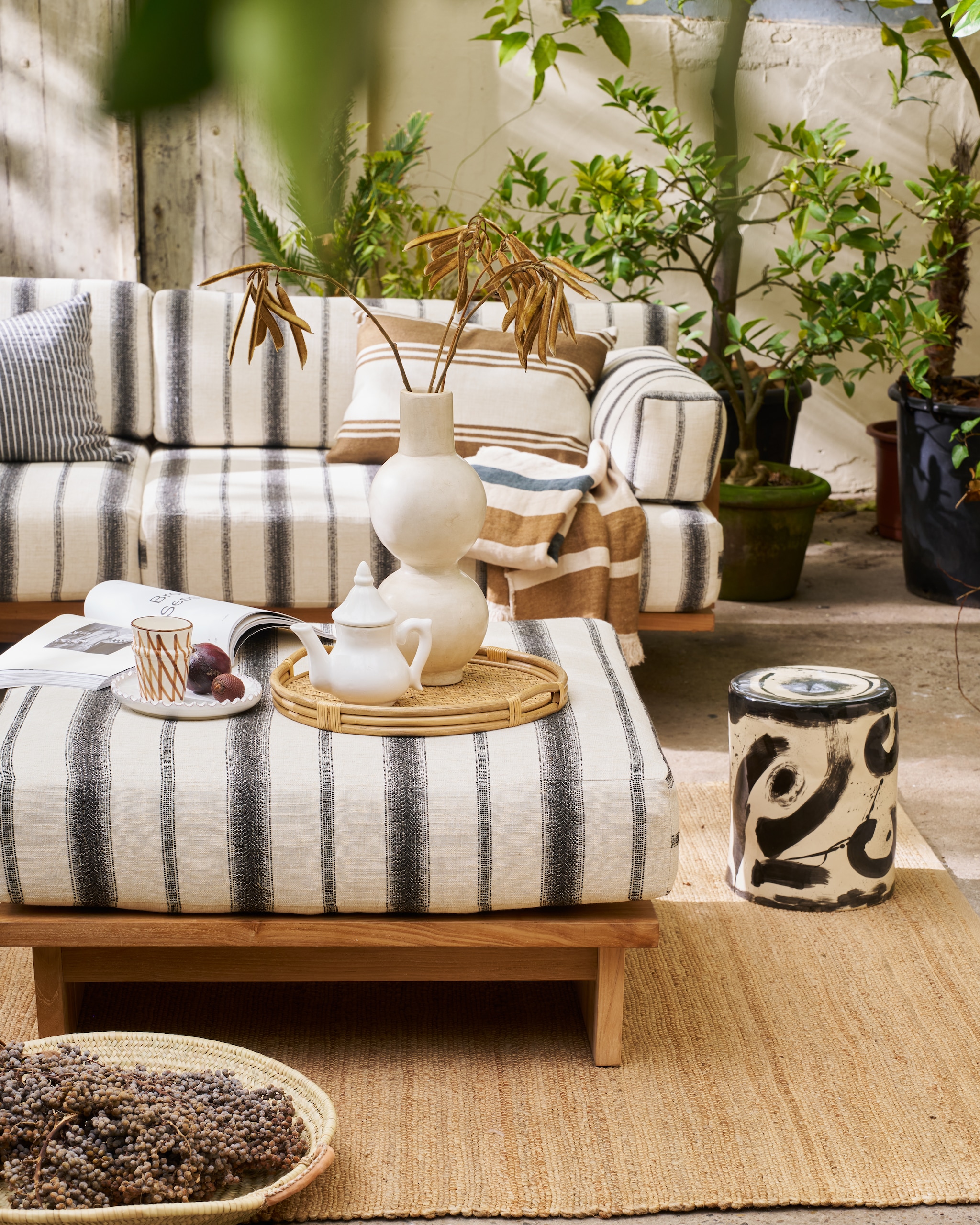 HKliving outdoorbank Chalkstripe, teak en outdoor stof, meerkleurig, 227x67x93,5 cm (bxdxh) € 3295,-, outdoor hocker Chalkstripe, teak en outdoor stof, meerkleurig, 88x88x38 cm (bxdxh) € 995,-, vloerkleed, jute, naturel, 340x240 cm (lxb) € 329,-, kussen Monochrome, zwart-wit gestreept € 54,90 (shop.vtwonen.nl). Household Hardware vaas Bubble, tadelakt, wit € 115,-, theepot, keramiek, wit € 49,-, bord, keramiek, wit € 25,-, schaal Marrakech, riet, naturel € 65,-,  (shop.vtwonen.nl). Omar Antwerp buitenkussen Olga, stof en dons, crème en bruin gestreept, inclusief vulling € 165,- en in 60x40 cm (bxh) inclusief vulling € 125,- (omar-antwerp.be). ’t Achterhuis potten, hout, bruin, vanaf € 150,-, mand, riet, naturel, vanaf € 200,- (achterhuis.nl). Serax bijzettafel 06 Sophia Pawn, ontworpen door Marie Michielsen, steengoed, zwart, 27x27x34 cm (bxdxh) € 190,- (serax.com). Libeco sierdeken Julian, linnen, gestreept € 396,- (libecohomestores.eu). Overig privébezit. vtwonen Landelijk 03-2026 | fotografie Jeroen van der Spek | styling Cleo Scheulderman