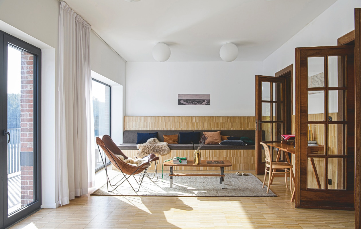 Bank en kussens op maat gemaakt. Tafel vintage. Sierkussens, vaas, leren vlinderstoel, leren kruk, telefoontasje, plafondlampen, schapenvacht, stoel, vaas, tafellamp, wandlamp en ledlampen Zangra. Bureau rommelmarktvondst. Foto oude ansichtkaart uitvergroot en op aluminiumplaat geplakt. Mand Blokker. vtwonen 12-2025 | styling Marit Saladini | fotografie Louis Lemaire