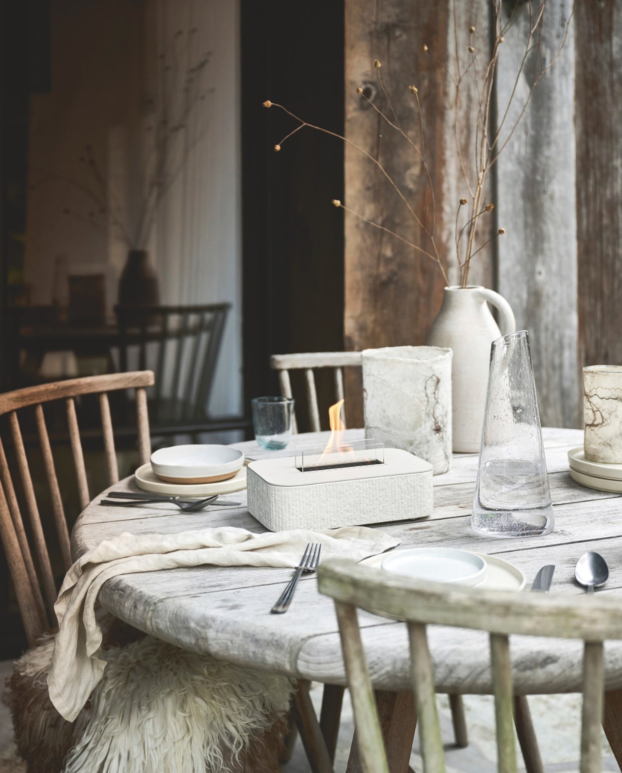 vtwonen tafelhaard Glow Aris 90, beton, beige, 25,5x16,1x12 cm (bxdxh) € 299,90.< M.m.v. vachtenspecialist.nl (krulschapenvacht), rawmaterials.eu (kan), zarahome.com (kom, bestek), sostrenegrene.com (servet). Overig privébezit. vtwonen landelijk 12-2025 | styling Sanne Ketelaar | fotografie Sjoerd Eickmans