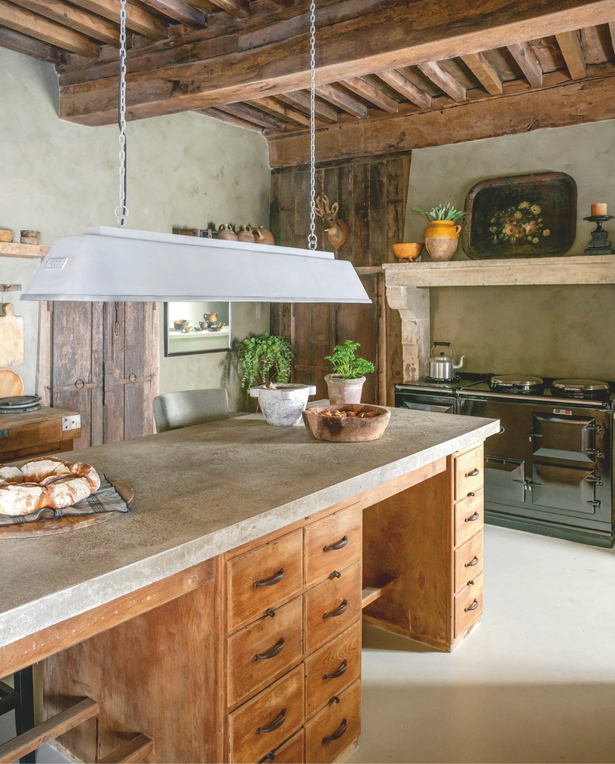 Keuken gemaakt door Reginald van gerecyclede materialen. Het eiland is een oud postkantoorbureau, werkblad van gegoten beton. Muurverf Tundra van Pure & Original. Hanglamp FrezoliLighting. Giclées van stillevens (gelimiteerde reproducties van schilderijen van de Nederlandse kunstenaar Henk Helmantel) Cerca Trova. vtwonen Landelijk 12-2025 | styling Amandine Berthon | fotografie Julien Fernandez