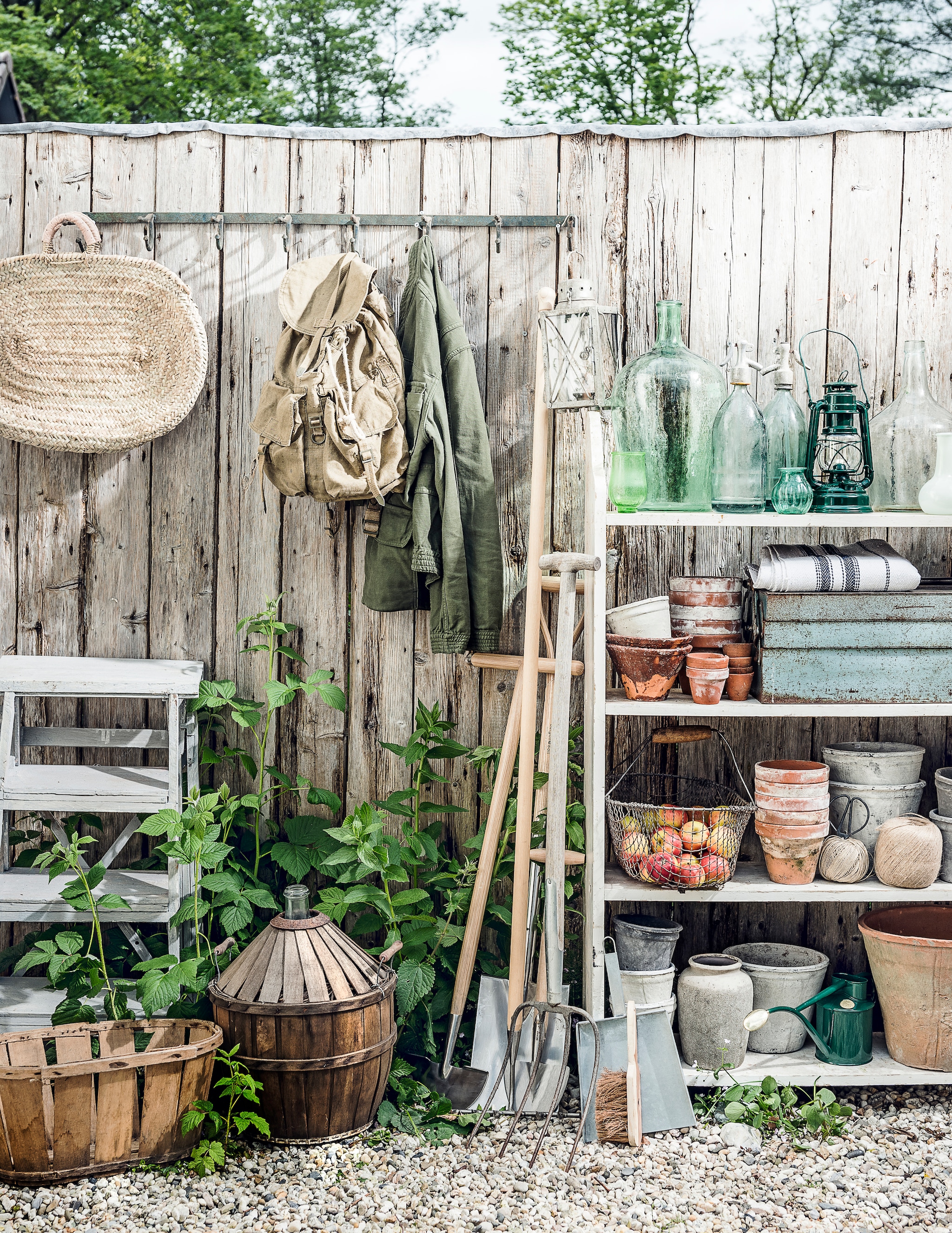 Trapje, stellingkast, fles in mand, rugzak, oude hark, groene vaas, glazen vaas, spuitflessen (Burbri Antiek). Kapstok, houten mand, oude lantaarn, kleine groene vaasjes, terracotta potten met bruin glazuur, witte bloempotten, grijze bloempot, grijze stenen vaas met ronde hals (De Weldaad). Rieten tas met leren details (Sukha Amsterdam). Jas, opgevouwen stof met blauwe streep (Six and Sons). Nieuw tuingereedschap, groene gieter (De Wiltfang). Handveger, veegblik (Loods 5). Groene lantaarn vanaf (Dille & Kamille). Terracotta bloempotten, oogstmand (Fleurmonde). Gereedschapskist (Brût Amsterdam). vtwonen special 01-2026 | fotografie Sjoerd Eickmans | styling Danielle Verheul