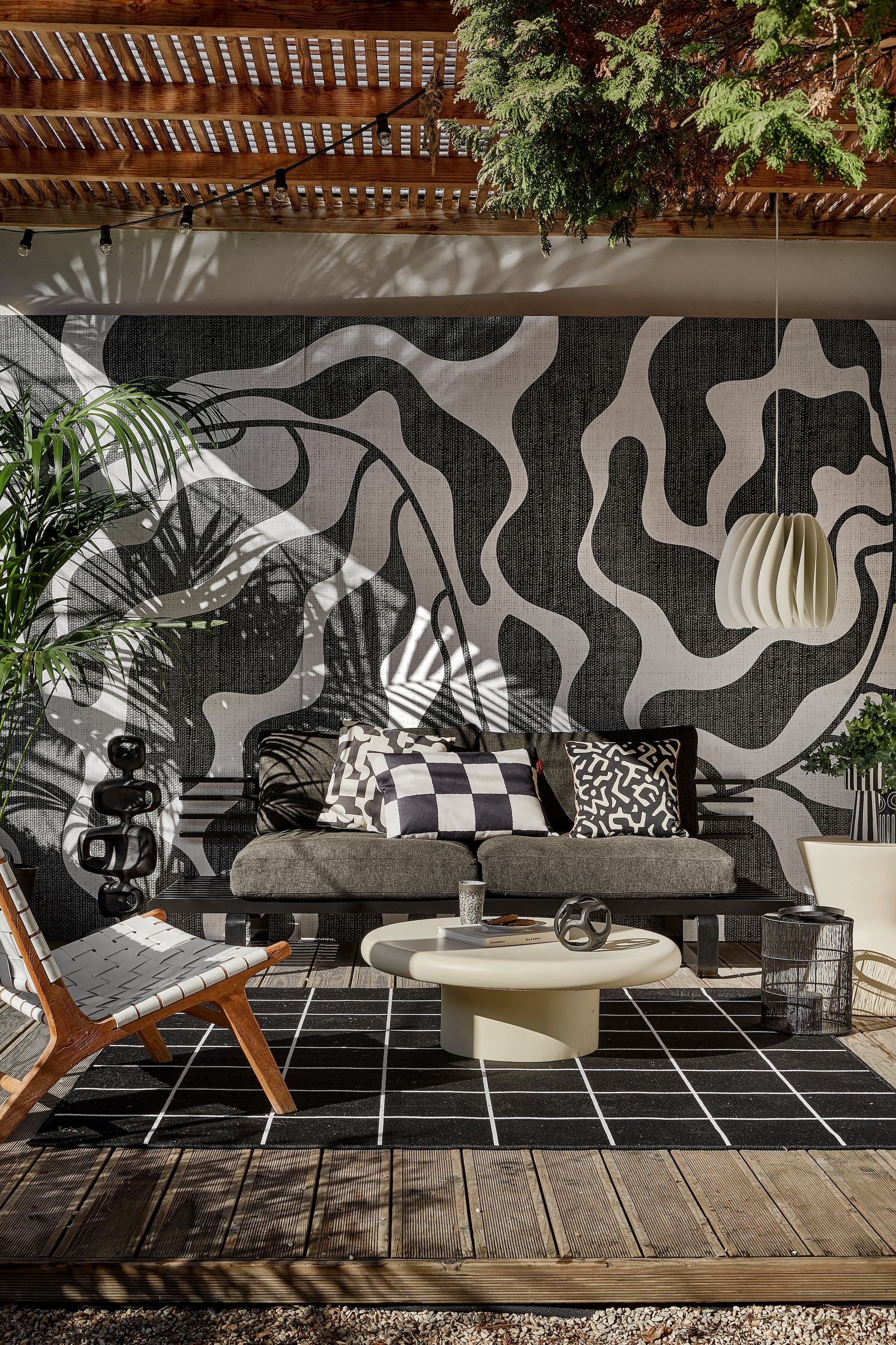 Behang River black & white van Wrap the Wall, per m2 € 150,-, minimale afname 4 m2 (behangfabriek.nl). Zwarte aluminium buitenbank € 1339,80, antraciet tuinkussens, per set € 675,75, zwarte aluminium sculptuur € 295,-, mok 70s, per 2 € 19,99 (hkliving.com). Buitenvloerkleed Svallerup, 200x200 cm € 79,95, hanglamp Skymningen € 79,95 (ikea.nl). Ivoorkleurige polyester bijzettafel, 85x30 cm (Øxh) € 599,-, bijzettafel Pot-Table in Ivory-Slim € 395,- (householdhardware.nl). Zwart-wit kussen Cutro € 10,- (kwantum.nl). Zwart-wit geblokt kussen King Pillow € 55,- (fatboy.com). Kussen Nara € 59,90 (ateliersem.nl). Zwart-wit gestreepte pot van Oyoy € 69,95, aardewerken vaas Troy van Bloomingville € 12,95 (livvlifestyle.nl). Zwart aluminium bolvormig ornament € 31,95, lantaarn € 96,95 (ptmd.nl). Fauteuil met gevlochten zitting privébezit, soortgelijke bij Kave Home (kavehome.com). vtwonen special 01-2026 | styling Kim Timmerman | fotografie Peggy Janssen